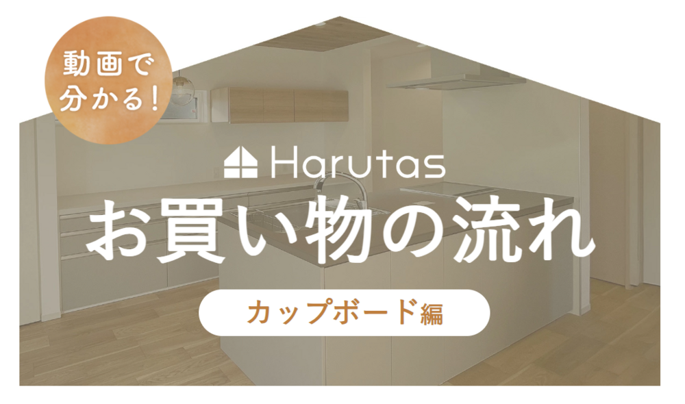 家型の枠内にアイランドキッチンの写真を背景として配置したタイトル画像。左上にオレンジ色の円形バッジで「動画で分かる！」の文字。中央にHarutasのロゴマークと社名、その下に大きく白文字で「お買い物の流れ」、さらに下に白い角丸バナーでオレンジ文字の「カップボード編」と表示されている。
