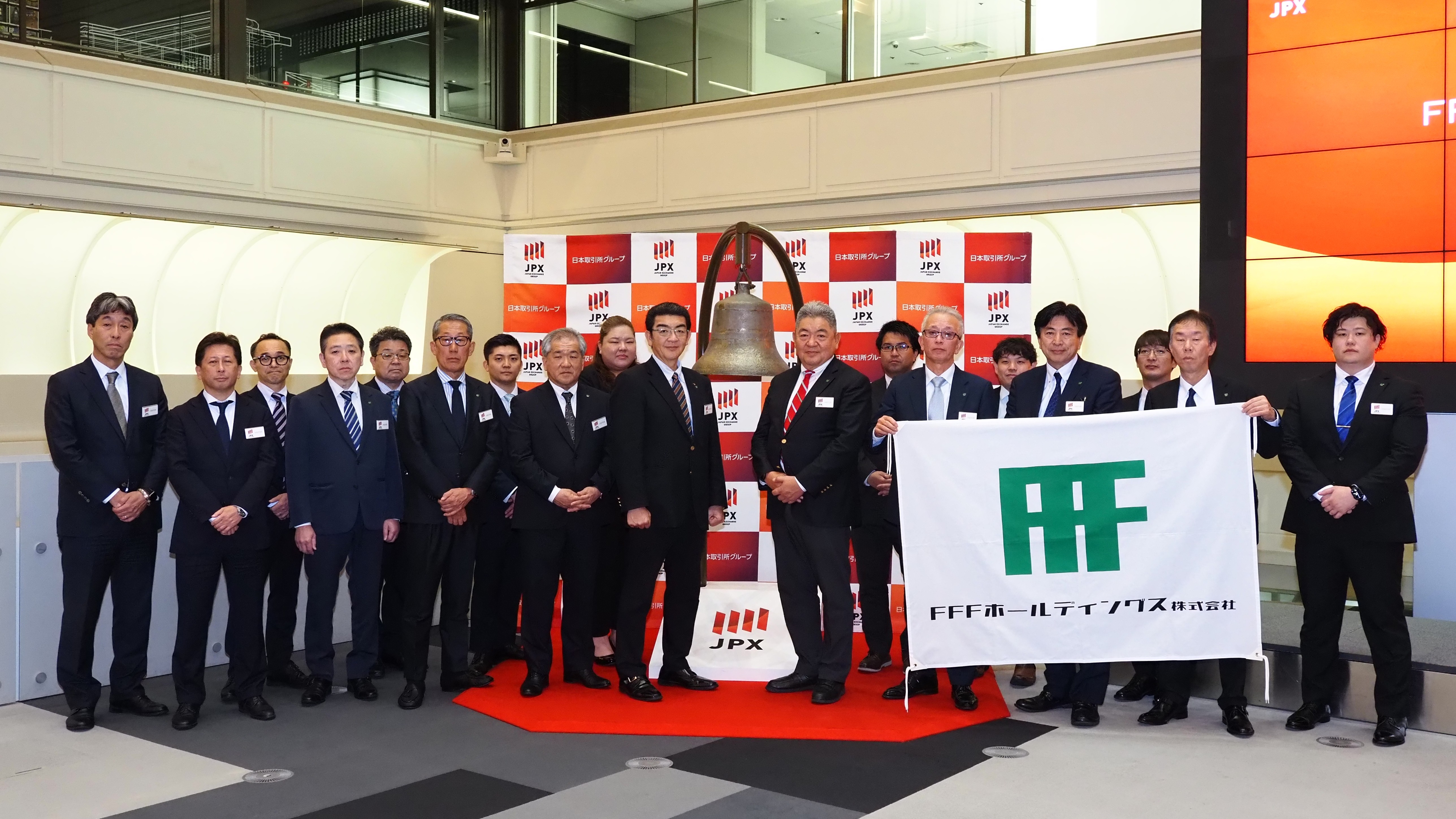東京証券取引所での上場セレモニーにて、上場の鐘を背に並ぶFFFホールディングス役職員一同の記念写真
