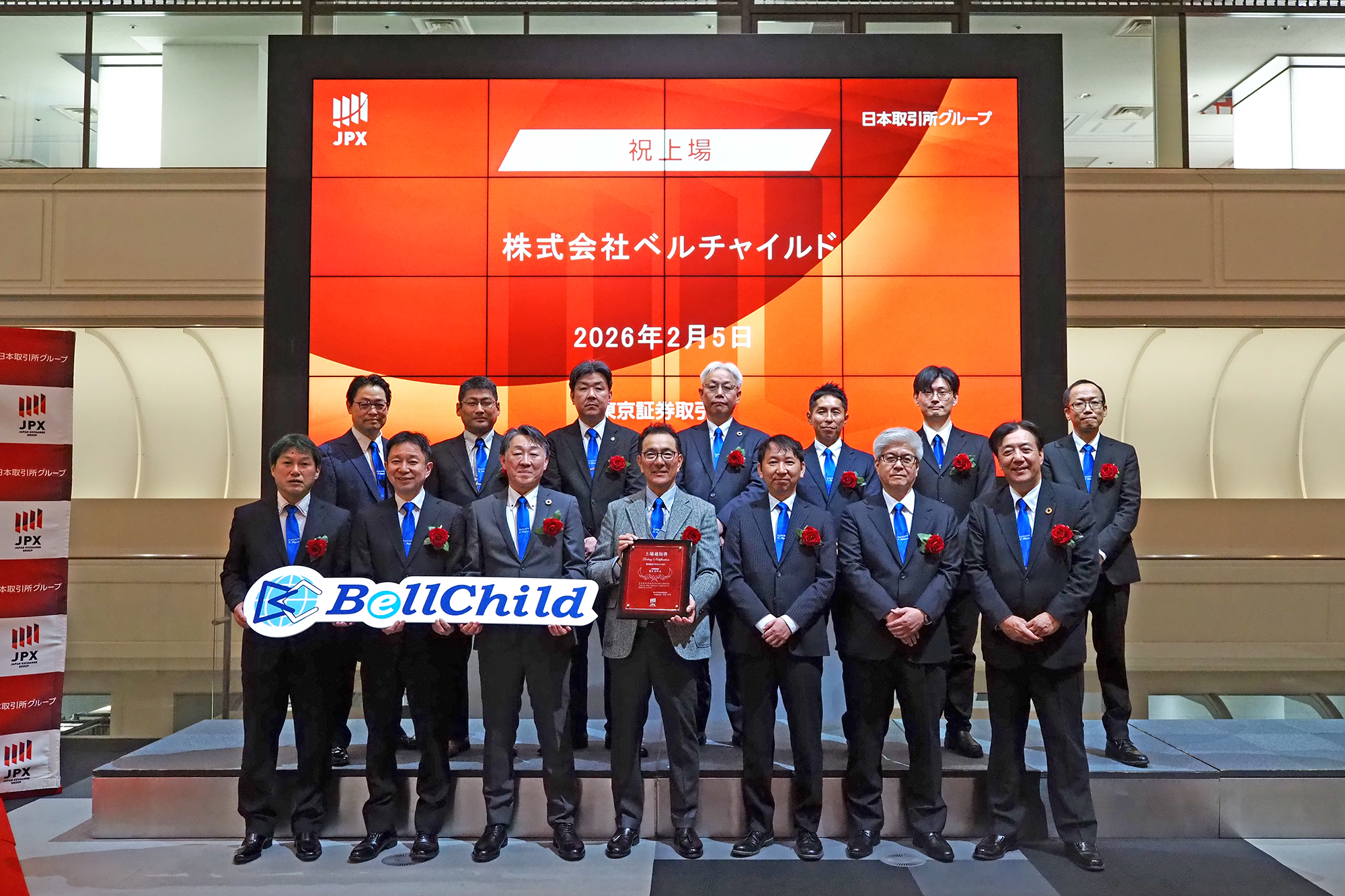 2026年2月5日、東京証券取引所での上場記念セレモニーにて、記念の上場通知書と社名パネルを手に並ぶ株式会社ベルチャイルドの役職員一行
