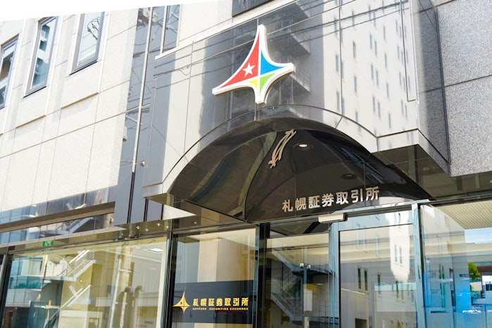 札幌証券取引所の建物外観。入り口の黒いひさしに「札幌証券取引所」の文字があり、上部には星マークがあしらわれたカラフルなロゴマークが掲げられている