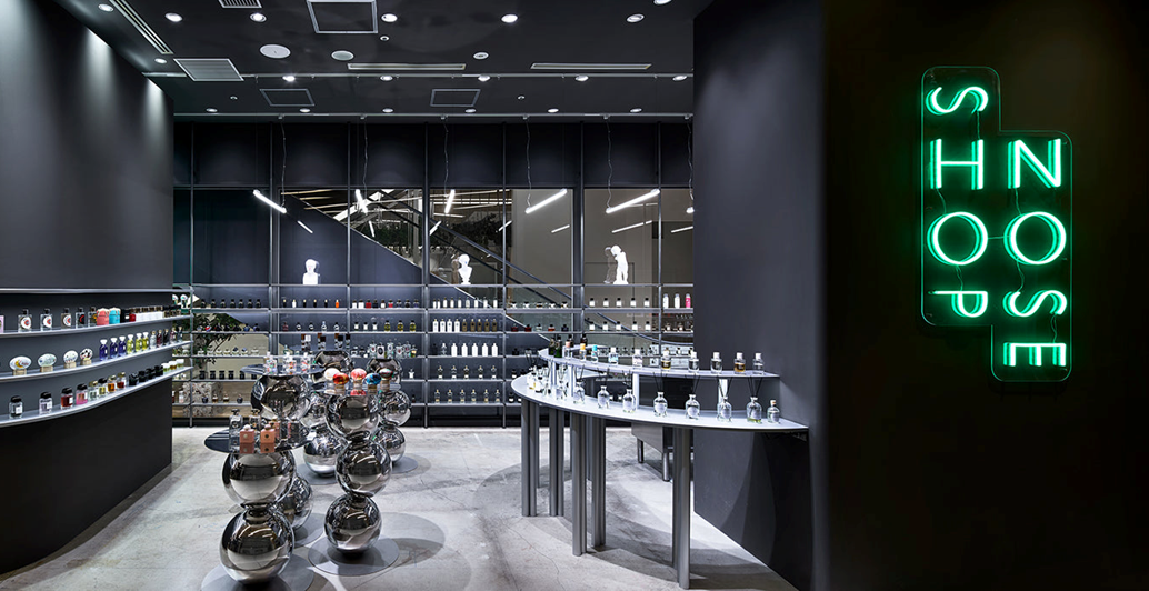 NOSE SHOPのグリーンに光るネオンロゴと、多数のフレグランスが整然と並ぶスタイリッシュな店舗内観のビジュアル