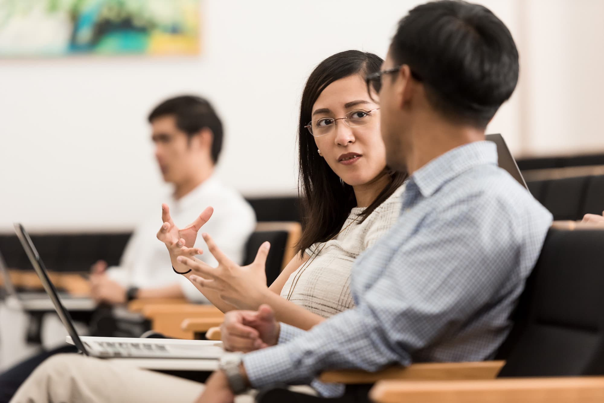 Two people are discussing and gesturing during a seated meeting.