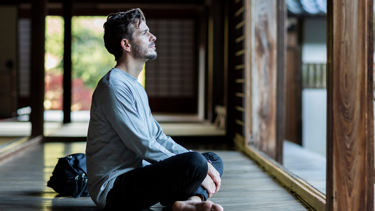 The image of a young professional sitting in quiet meditation along a traditional wooden corridor.