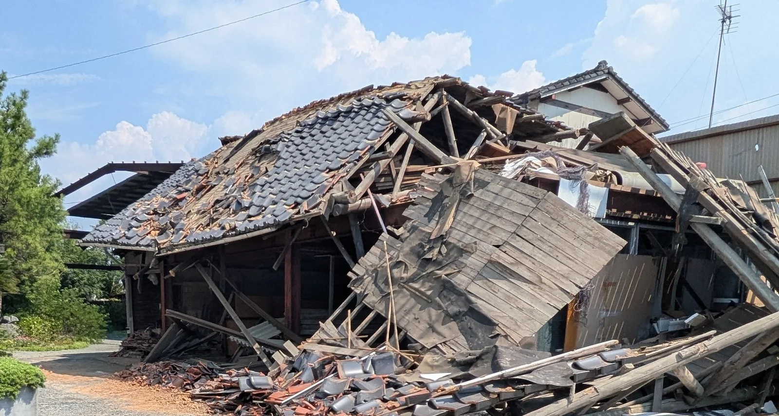 倒壊した木造の建物。屋根が崩れ落ち、瓦や木材が敷地の外の地面まで散乱している