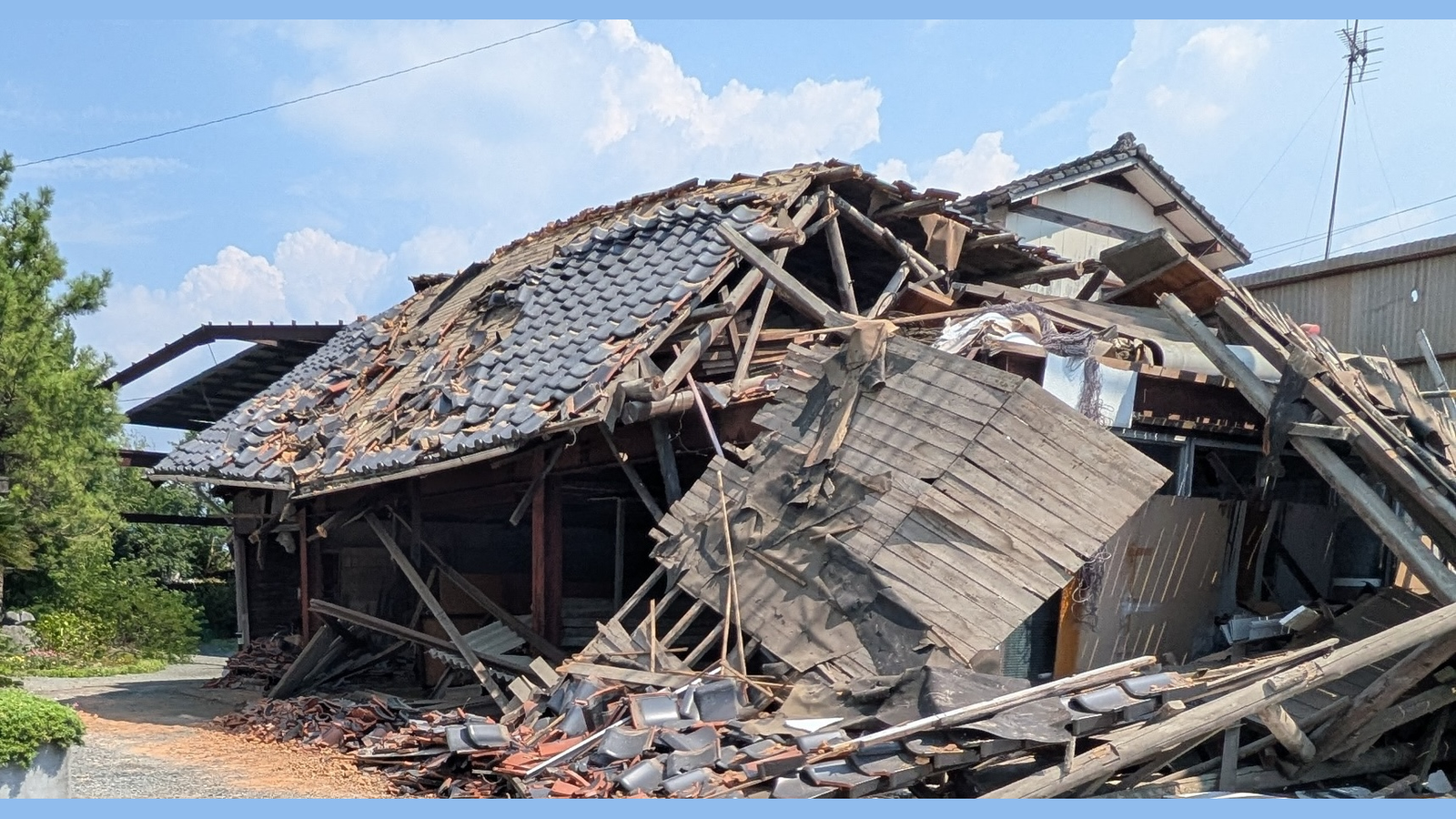 倒壊した木造の建物。屋根が崩れ落ち、瓦や木材が敷地の外の地面まで散乱している