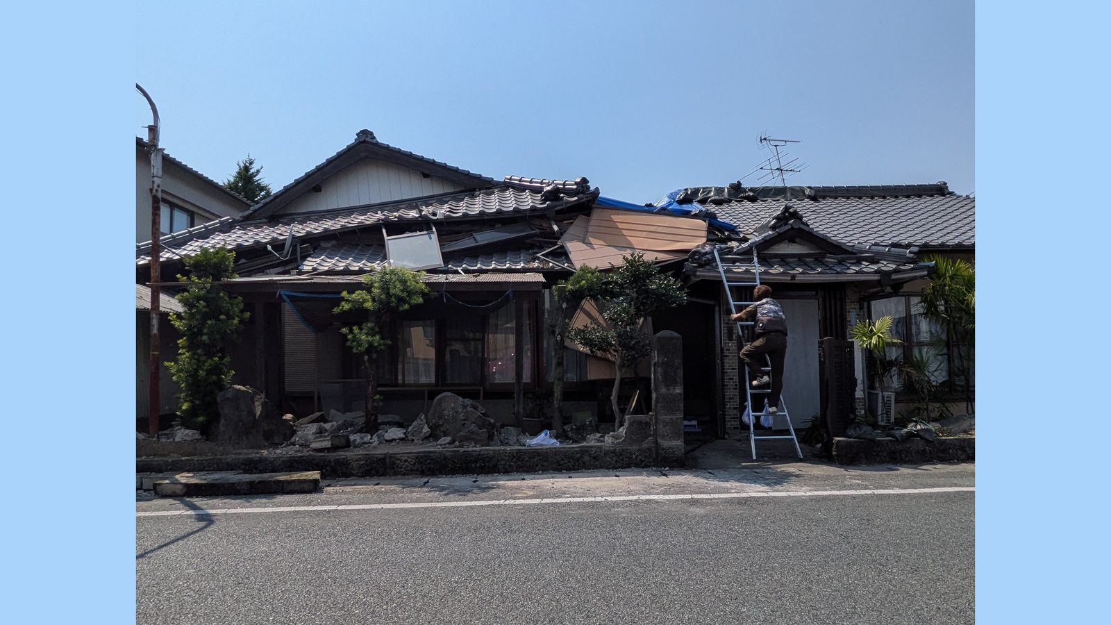屋根にシートがかけられた住宅。立てかけられたはしごを人が上っている
