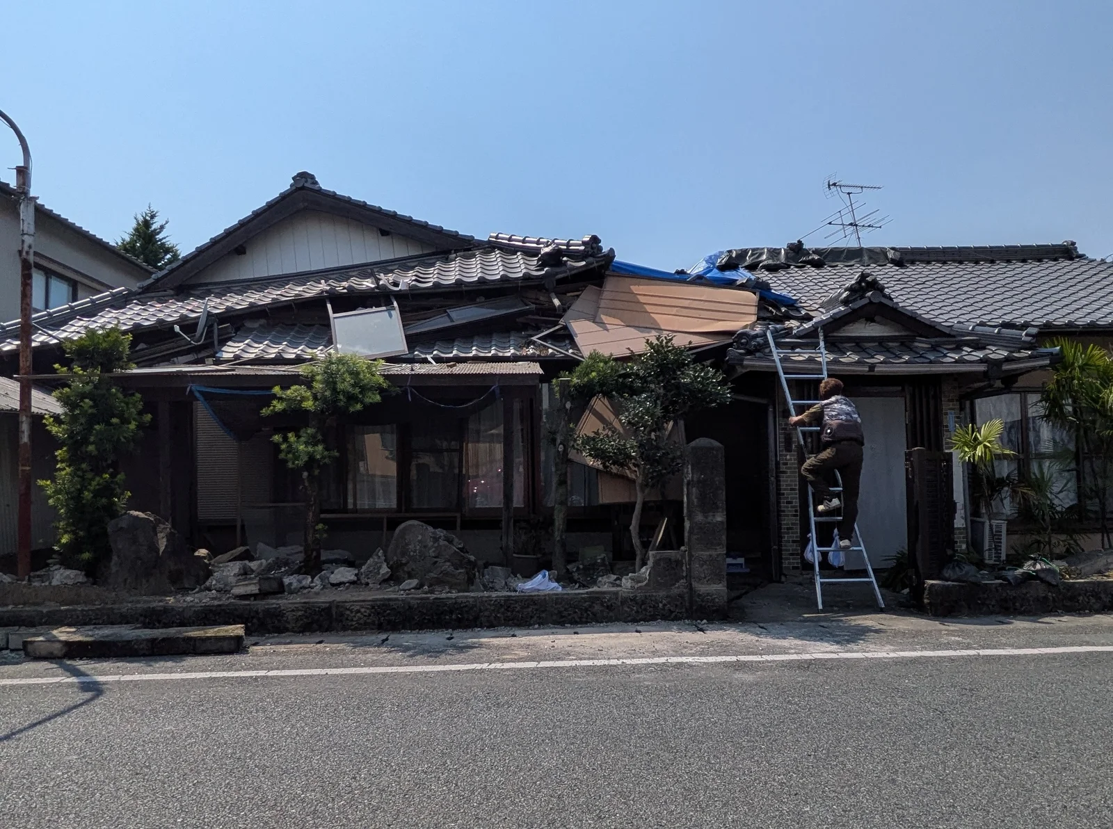 屋根にシートがかけられた住宅。立てかけられたはしごを人が上っている