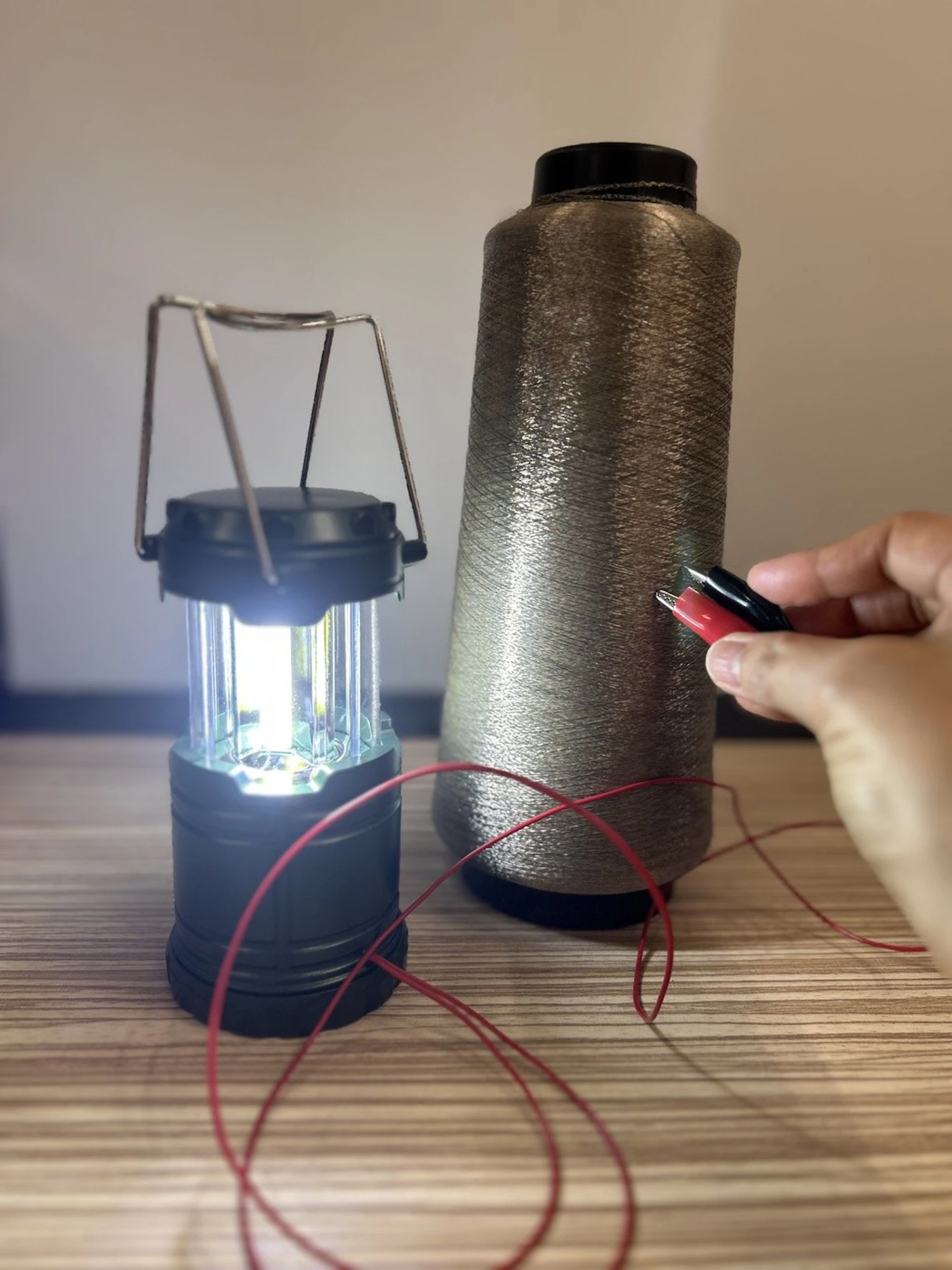 銀めっき繊維「AGposs®」の導電性を示す簡易試験。糸に電極を当てるとランタンが点灯する。電気を通す性能は数値で測定・証明できる