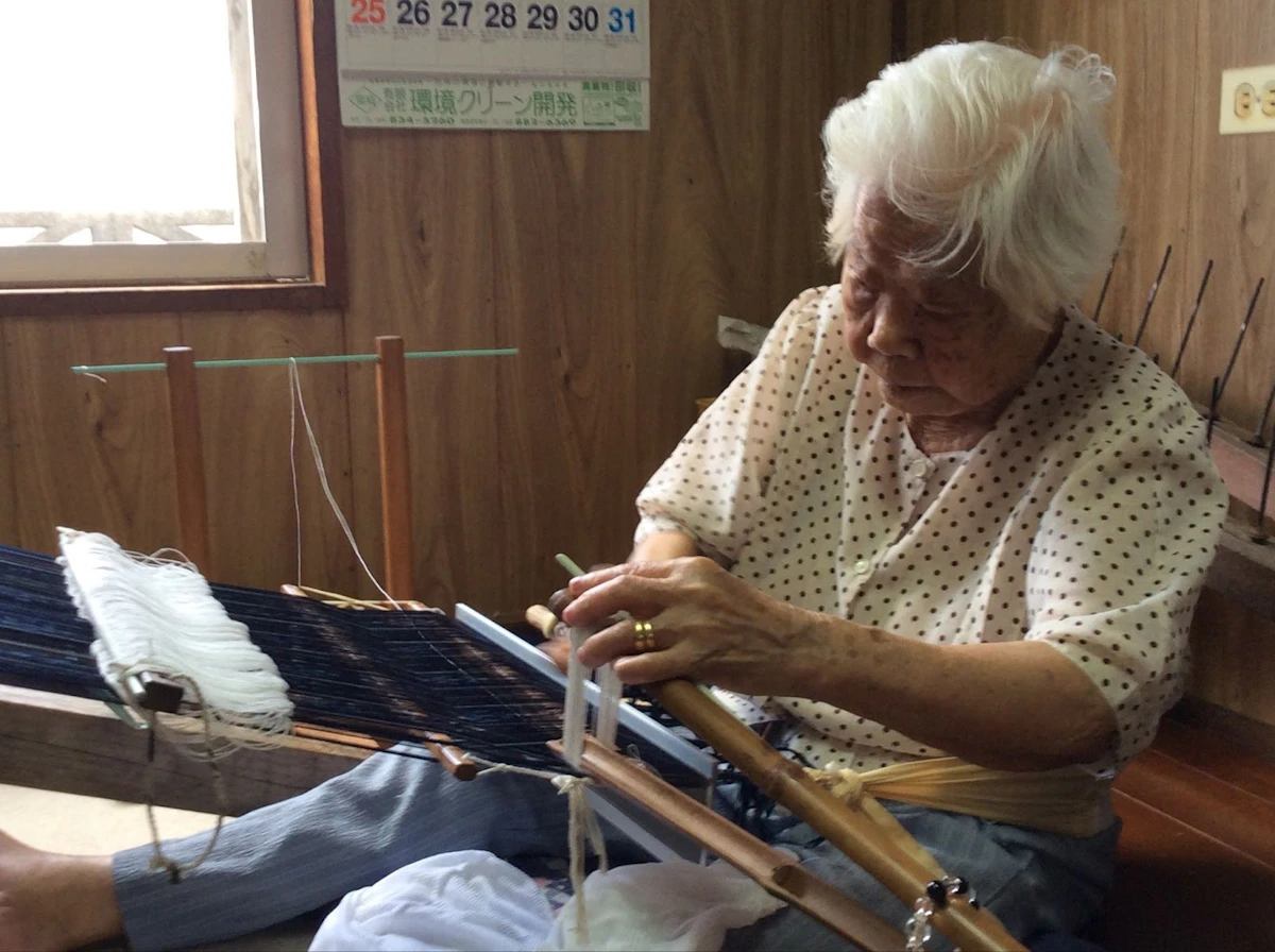 大城さんのおばあ（祖母）がヒャーカキ（綜絖掛け）をしている様子。現在は行っていないが、丸正織物工房が残していきたい技術としている。