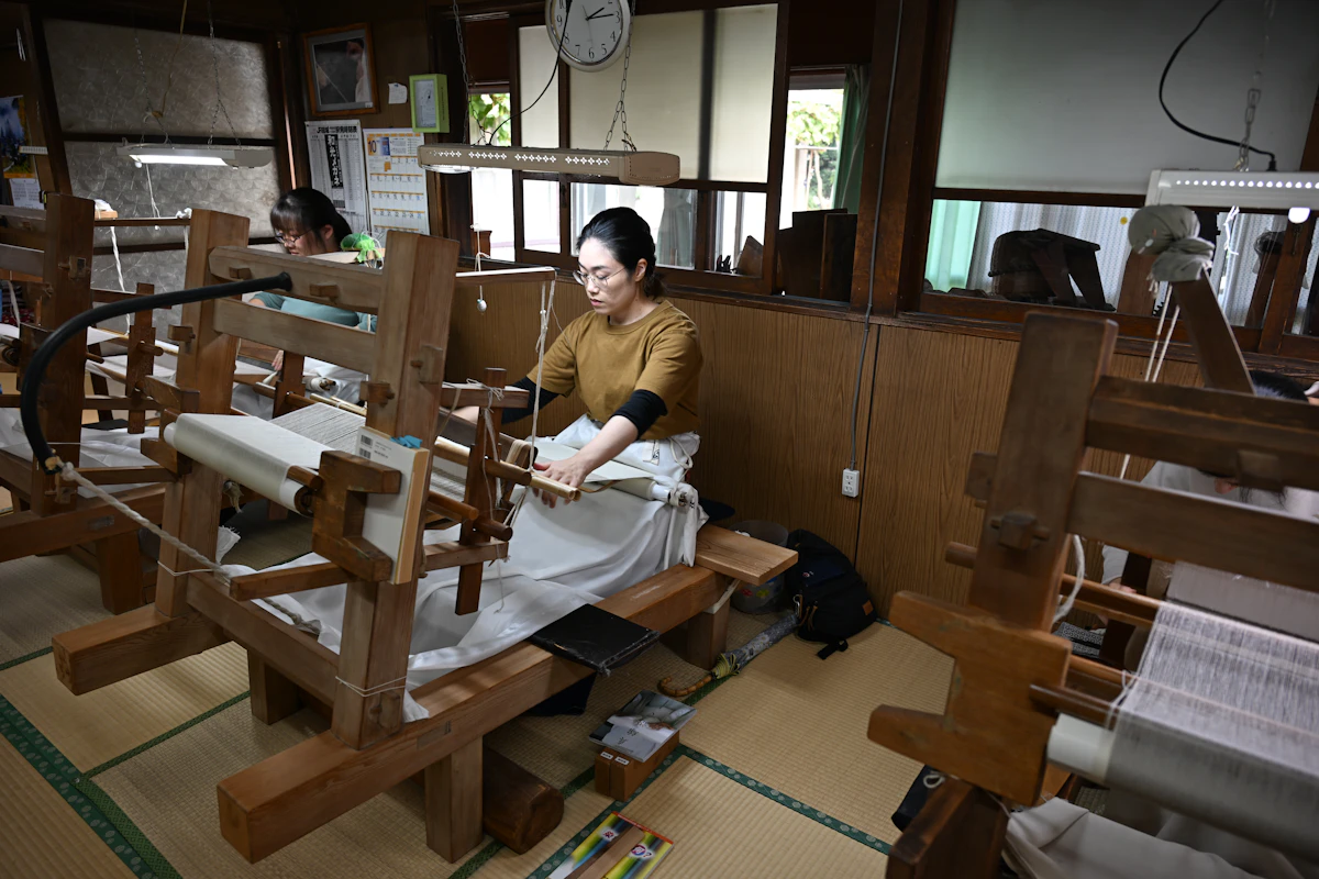 経糸（たていと）を腰に巻き付け、自分の体重で張り具合を調節しながら手で織り上げる「地機織り」