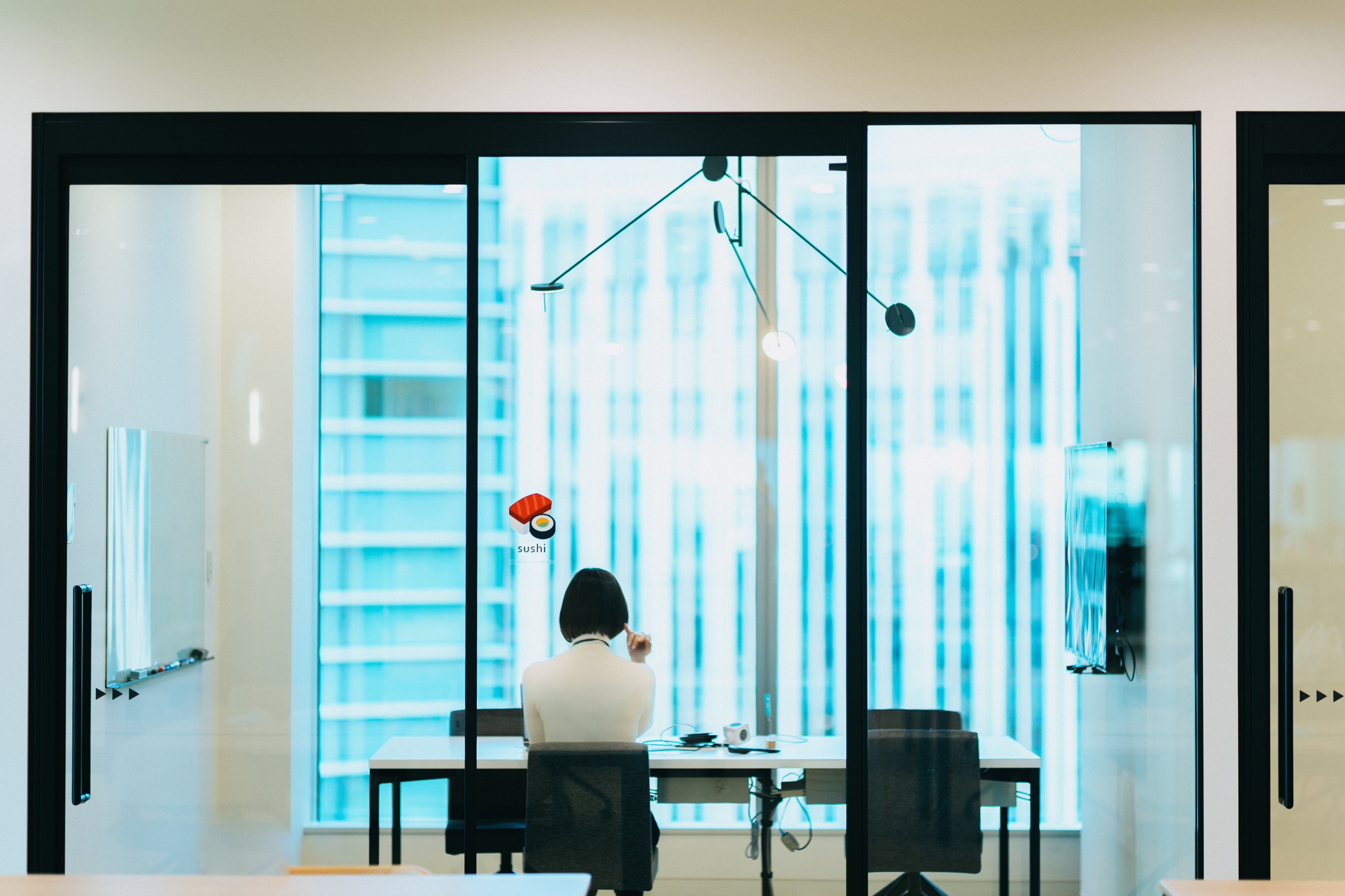 ガラス張りの会議室に一人座る社員の後ろ姿の写真