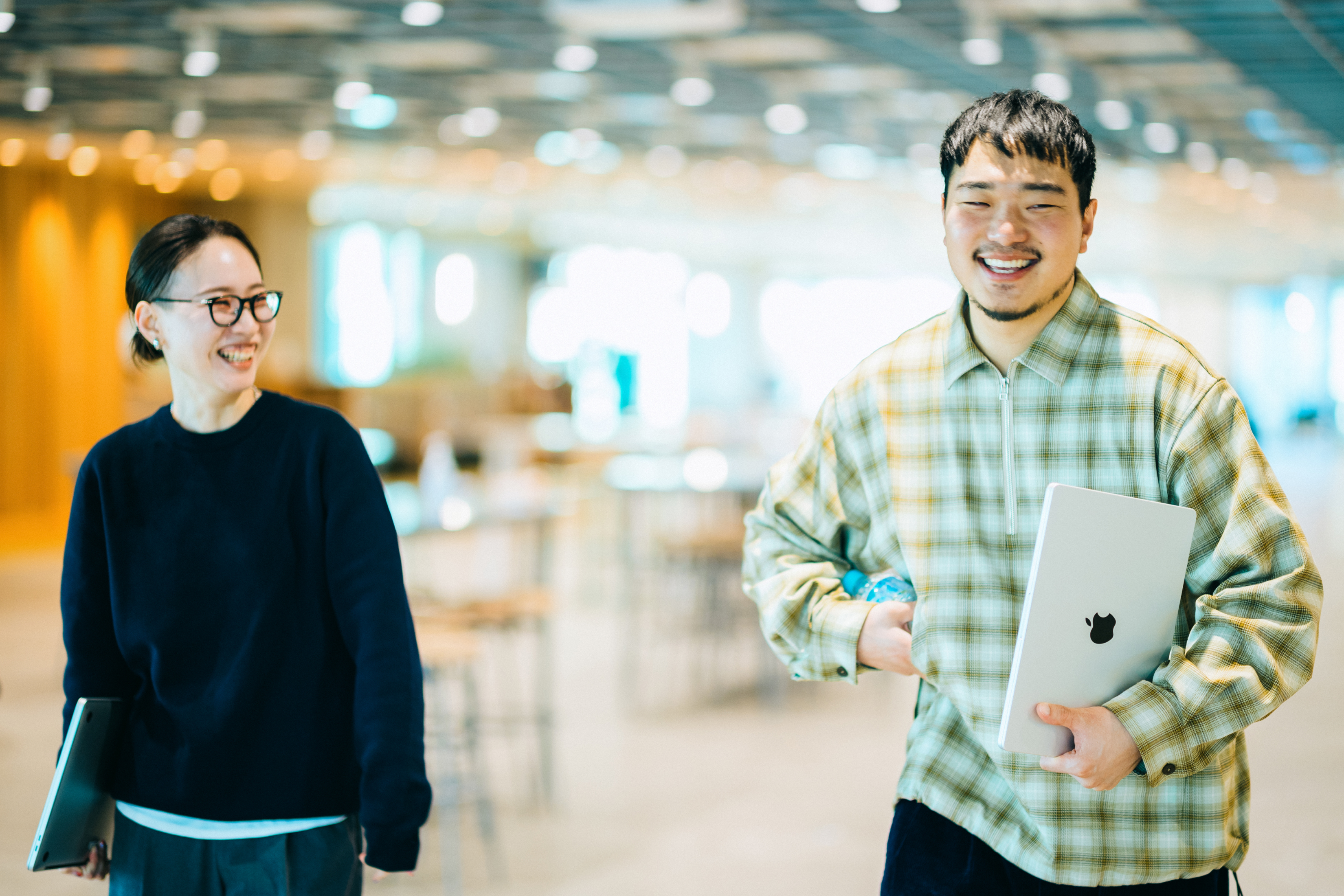 ラップトップパソコンを持って談笑しながら歩く2名の写真