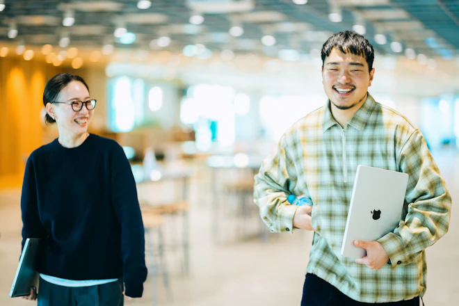 ラップトップパソコンを持って談笑しながら歩く2名の写真