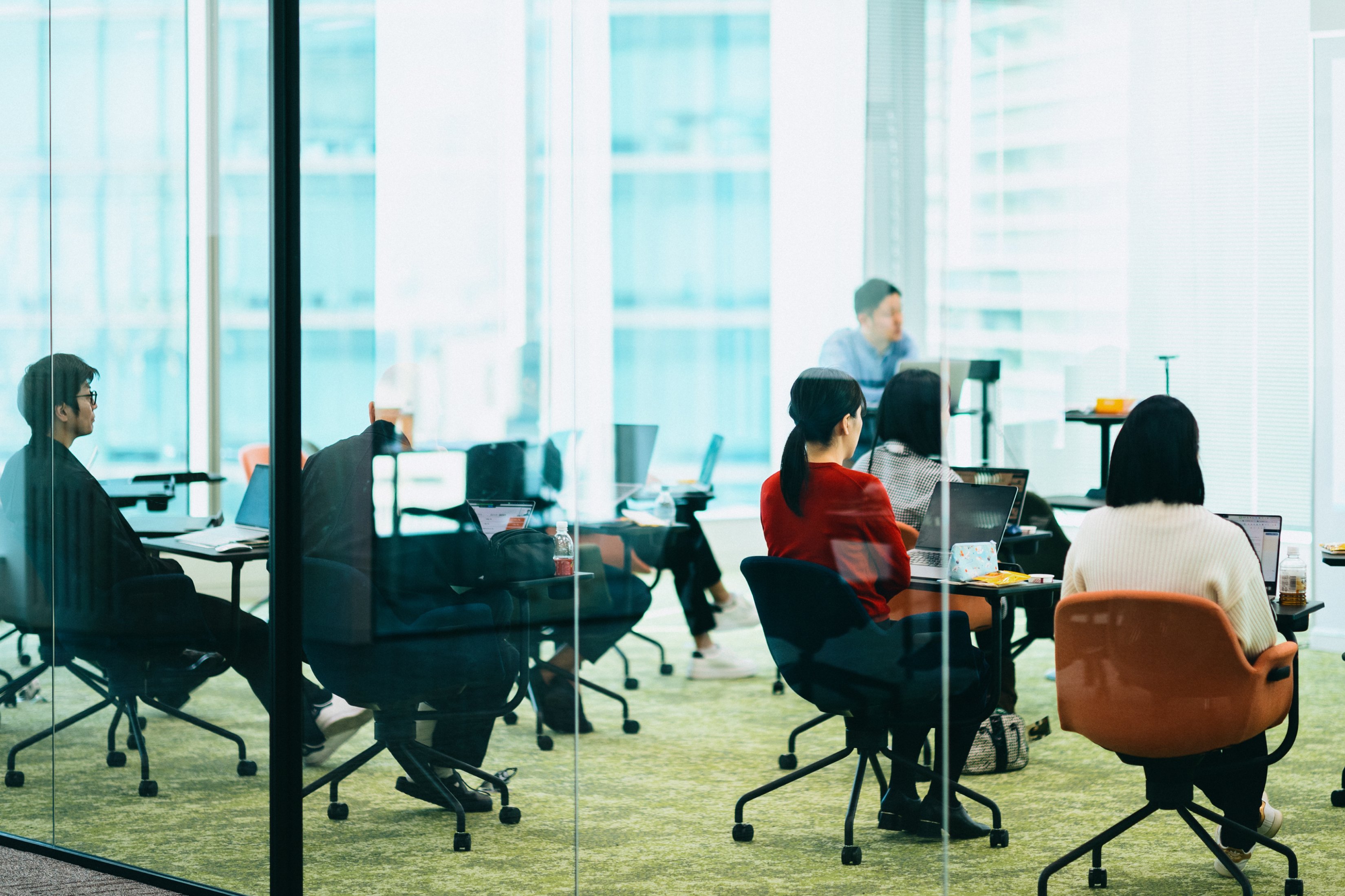 ガラス張りのエリアで皆同じ方向を向いて話を聞いている社員の写真