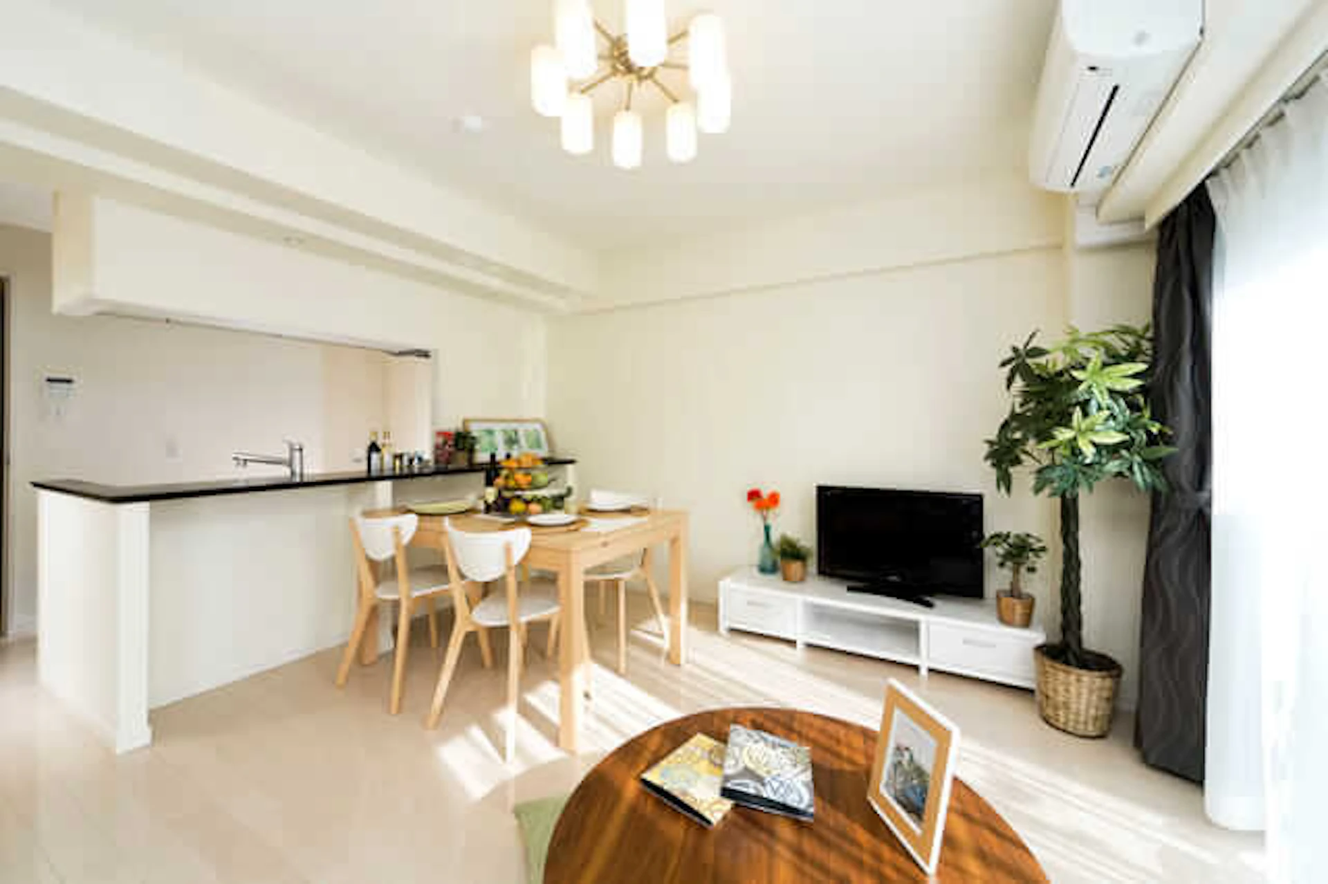 白い壁と白っぽいフローリングのダイニング、カウンターキッチンとダイニングテーブルセットがある