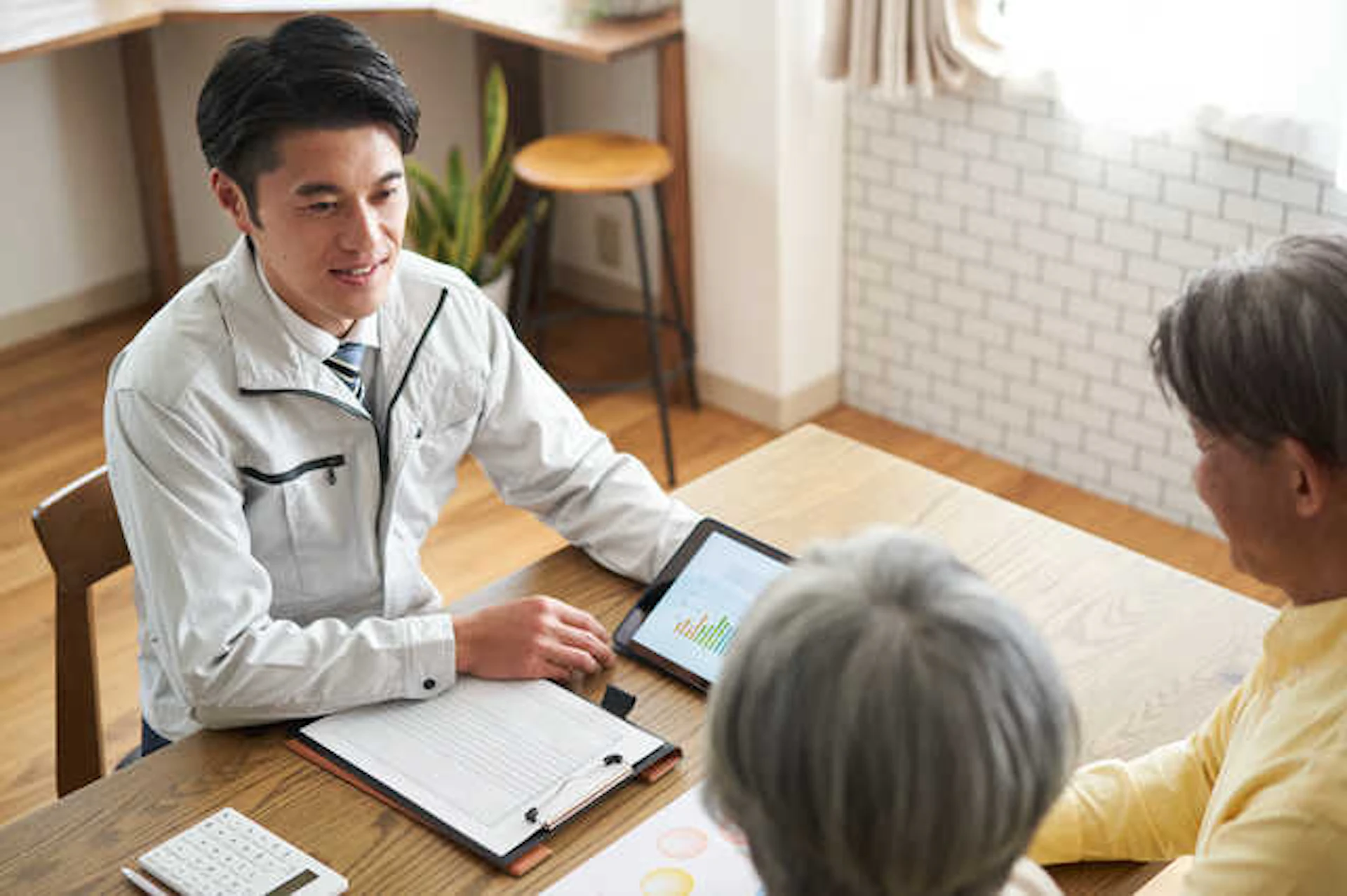 夫婦と向かい合わせに座って説明をする業者の男性