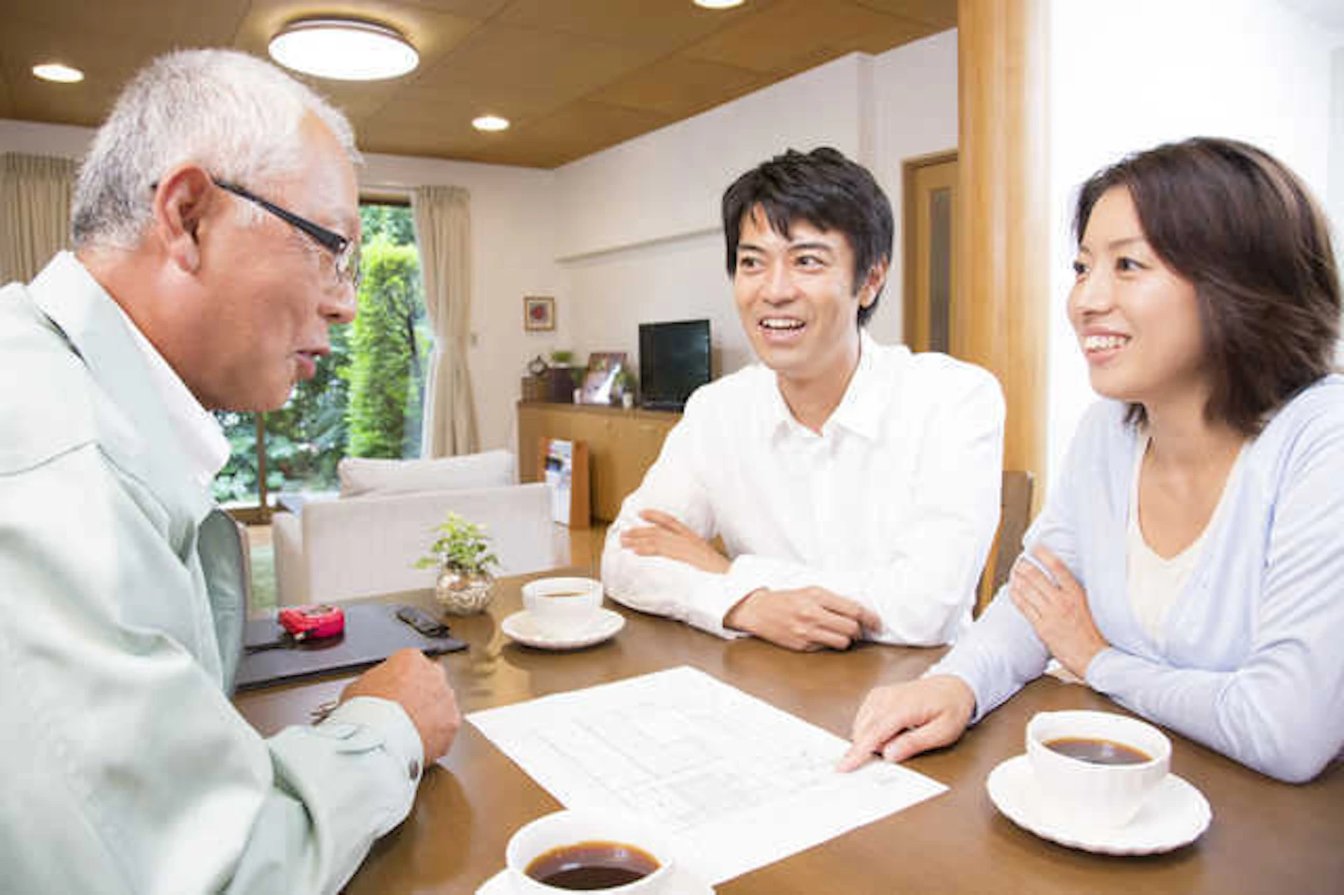 居間で相談している若い夫婦とリフォーム業者のシニア男性