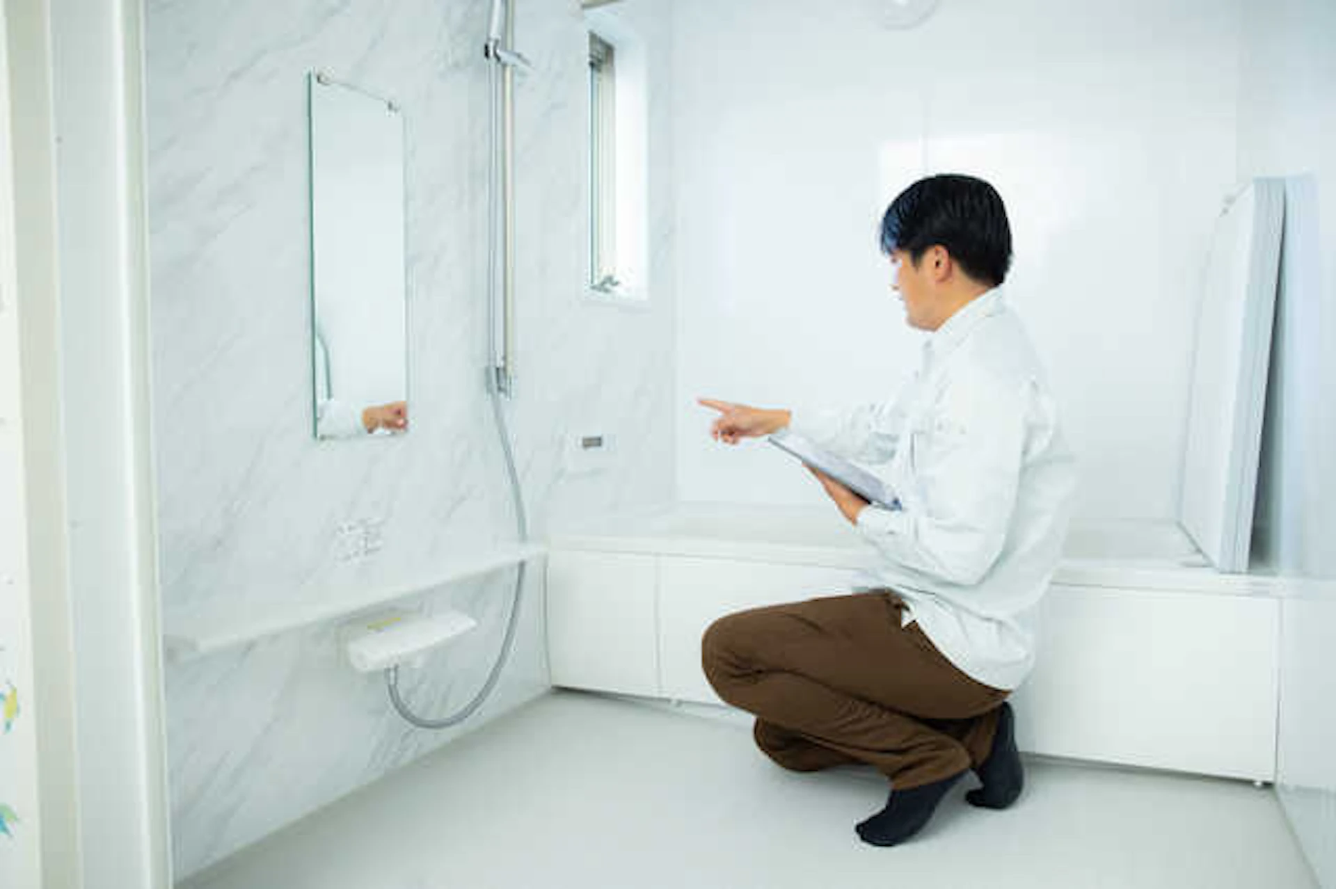 浴室の白い代理石模様シャワーがついた壁を点検する作業員の男性