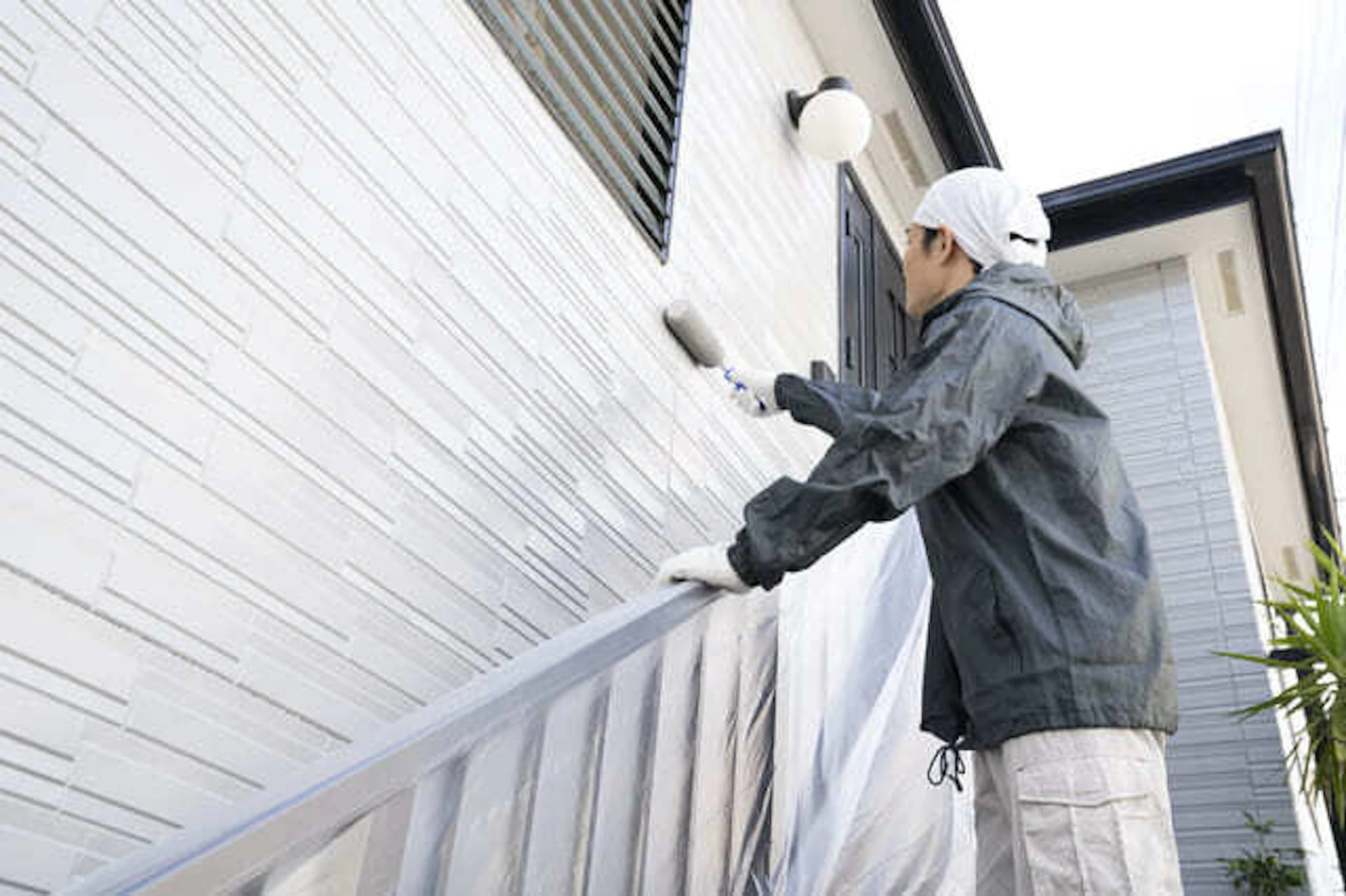 戸建て住宅の外壁をローラーで塗る職人の写真