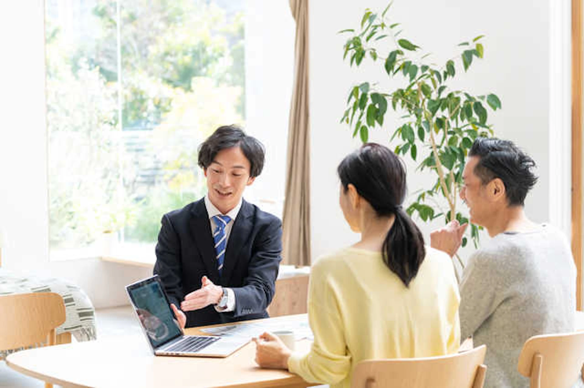 夫婦にパソコンの画面を見せる、スーツ姿の男性