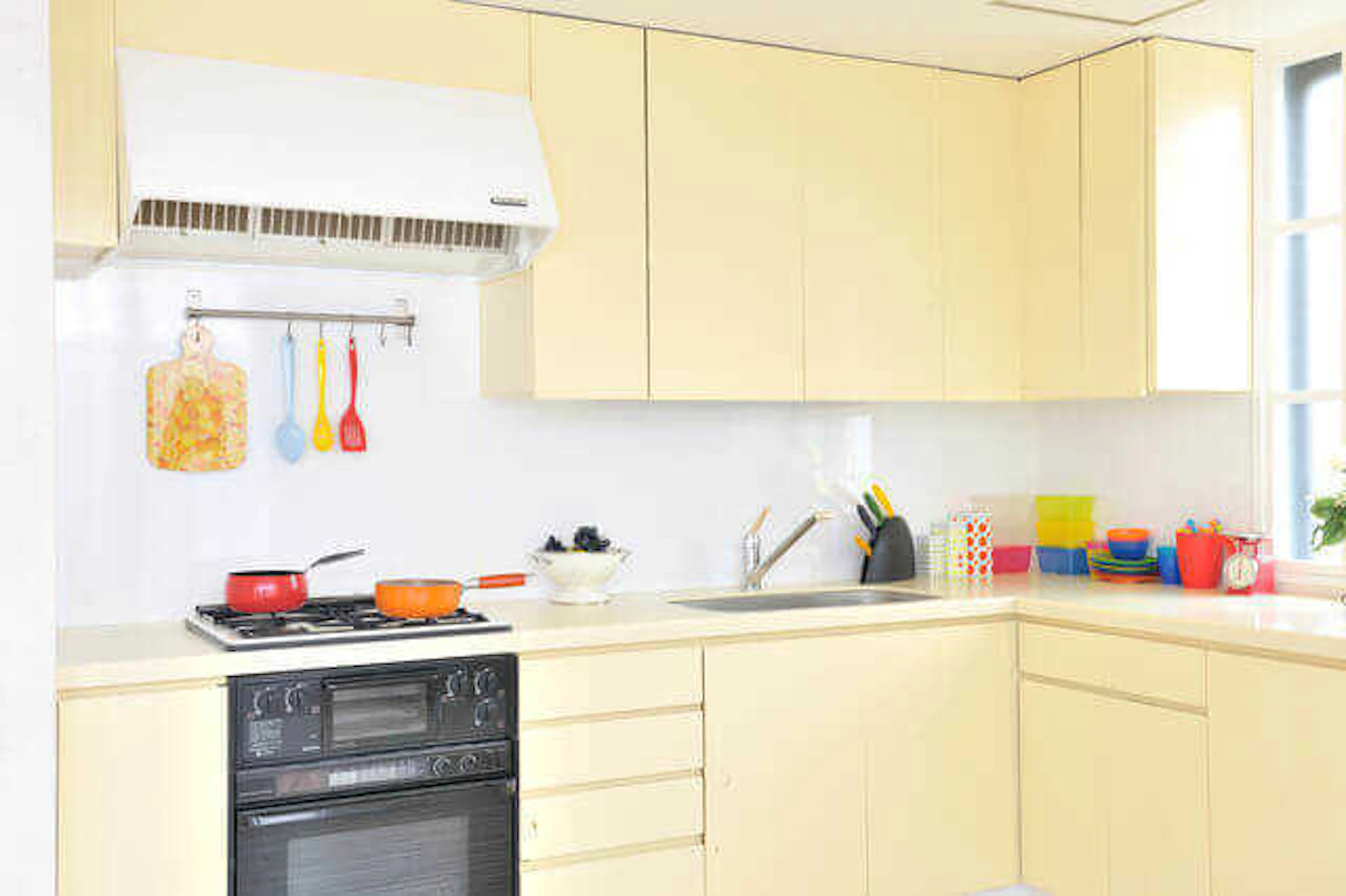カラフルな調理器具が並ぶ黄色基調のL型キッチンの写真