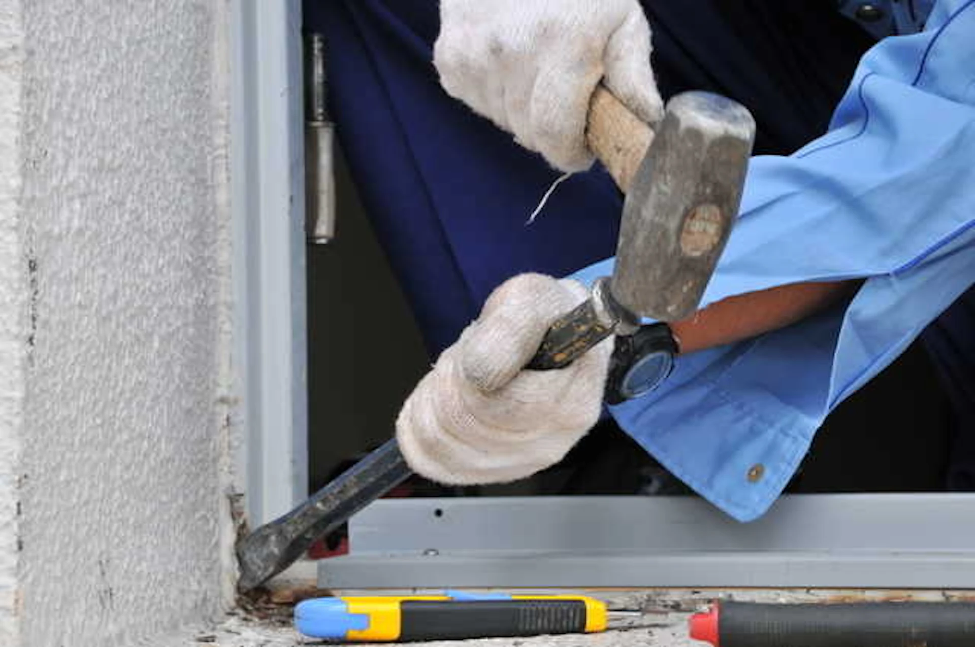 窓枠をピックとハンマーで工事する作業員の手元