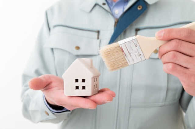 小さい家とハケを持っている男性作業員の写真