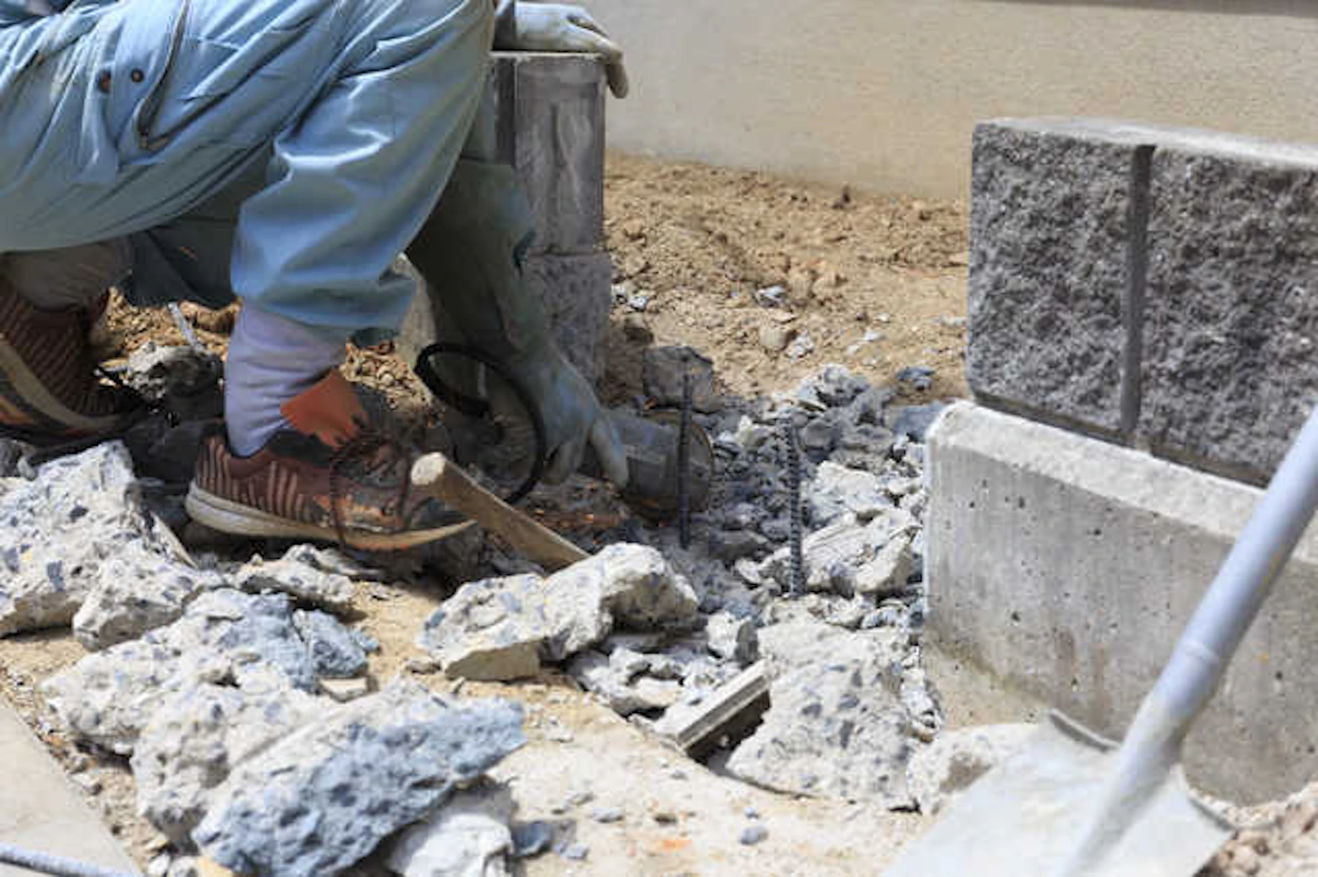 コンクリートのブロック壁を壊す水色の服をきた作業員の足元