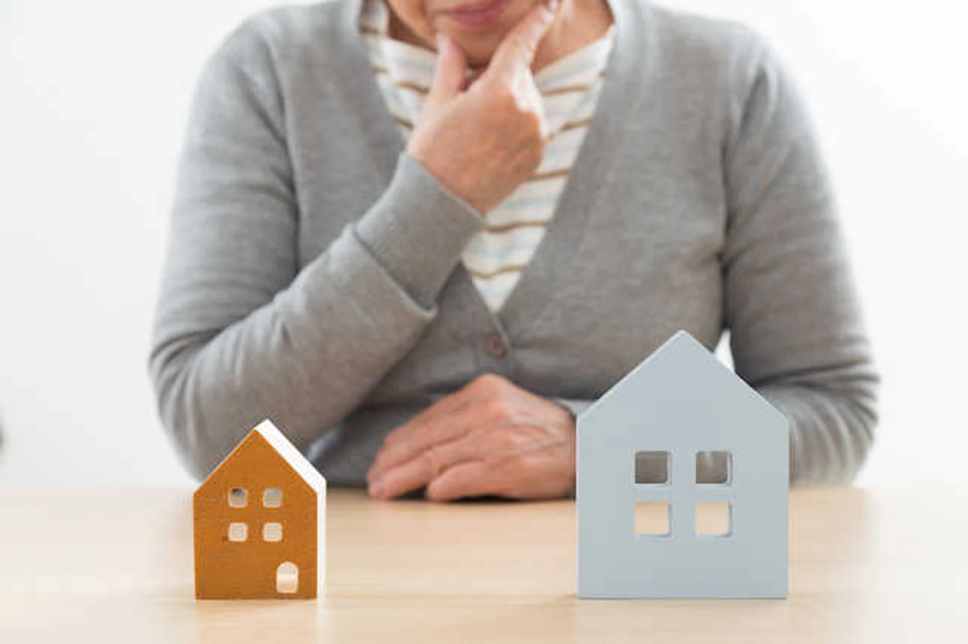 二つの家の模型を眺めながら考える女性