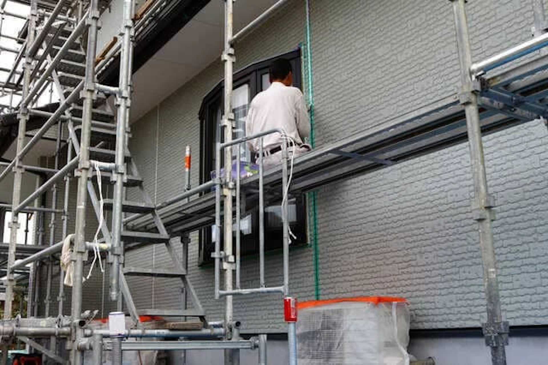 足場に腰かけて外壁の工事を進める男性作業員