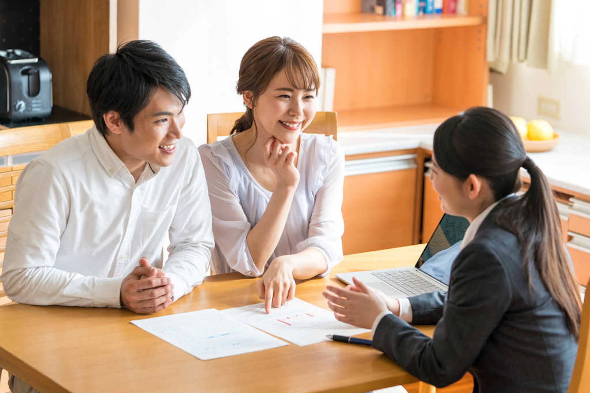 スーツを着た女性の説明を聞く若い夫婦