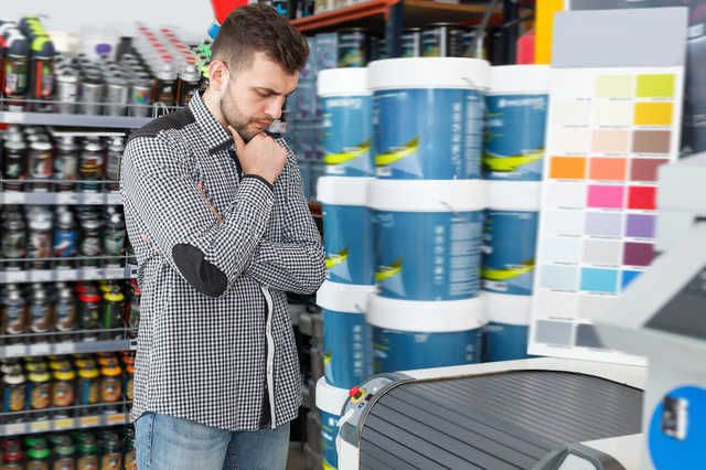 塗料屋で塗料を前にどれを選ぶか迷っている男性