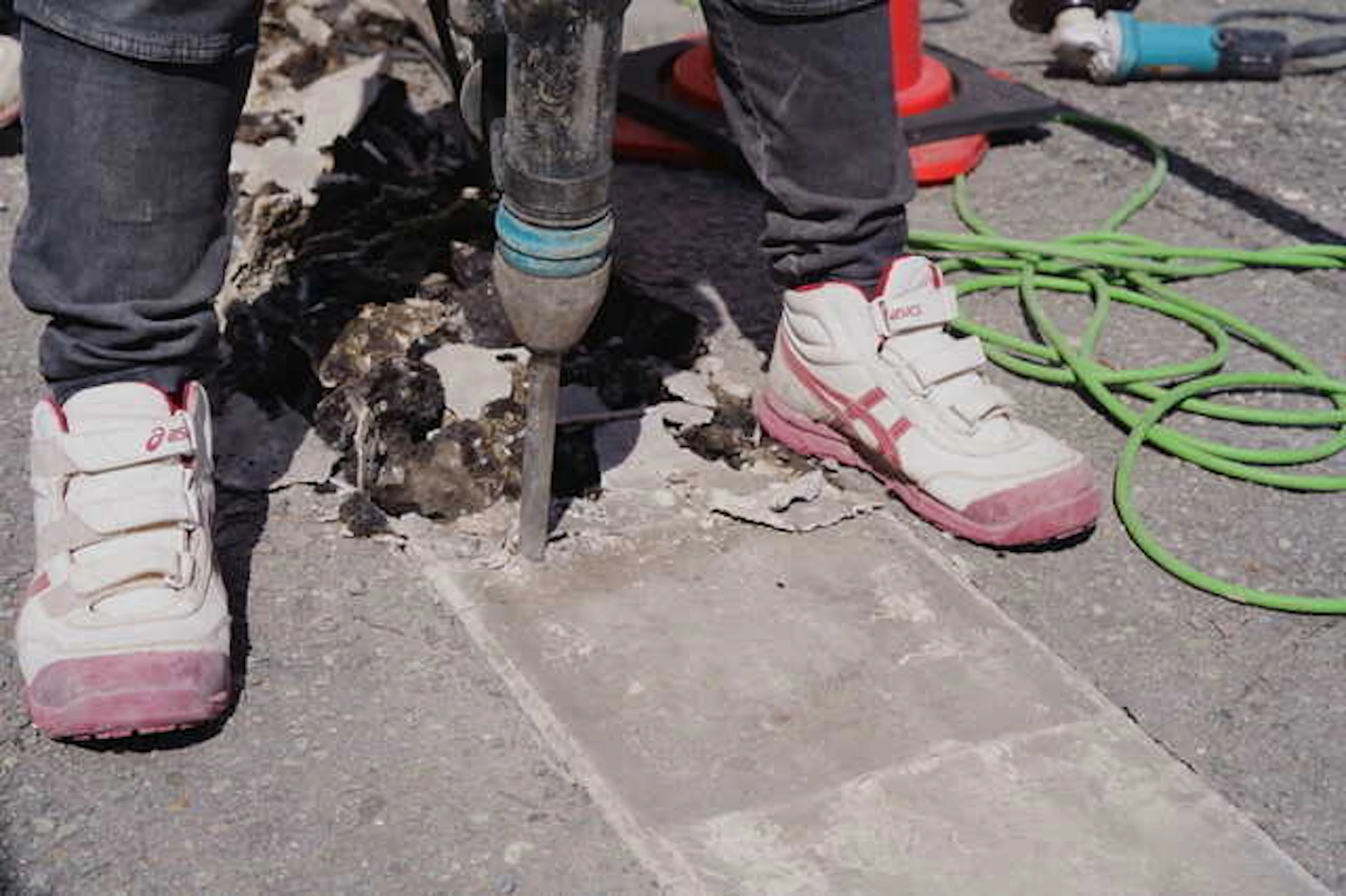 道路のコンクリートを機械で壊すスニーカーを履いた作業員の足元