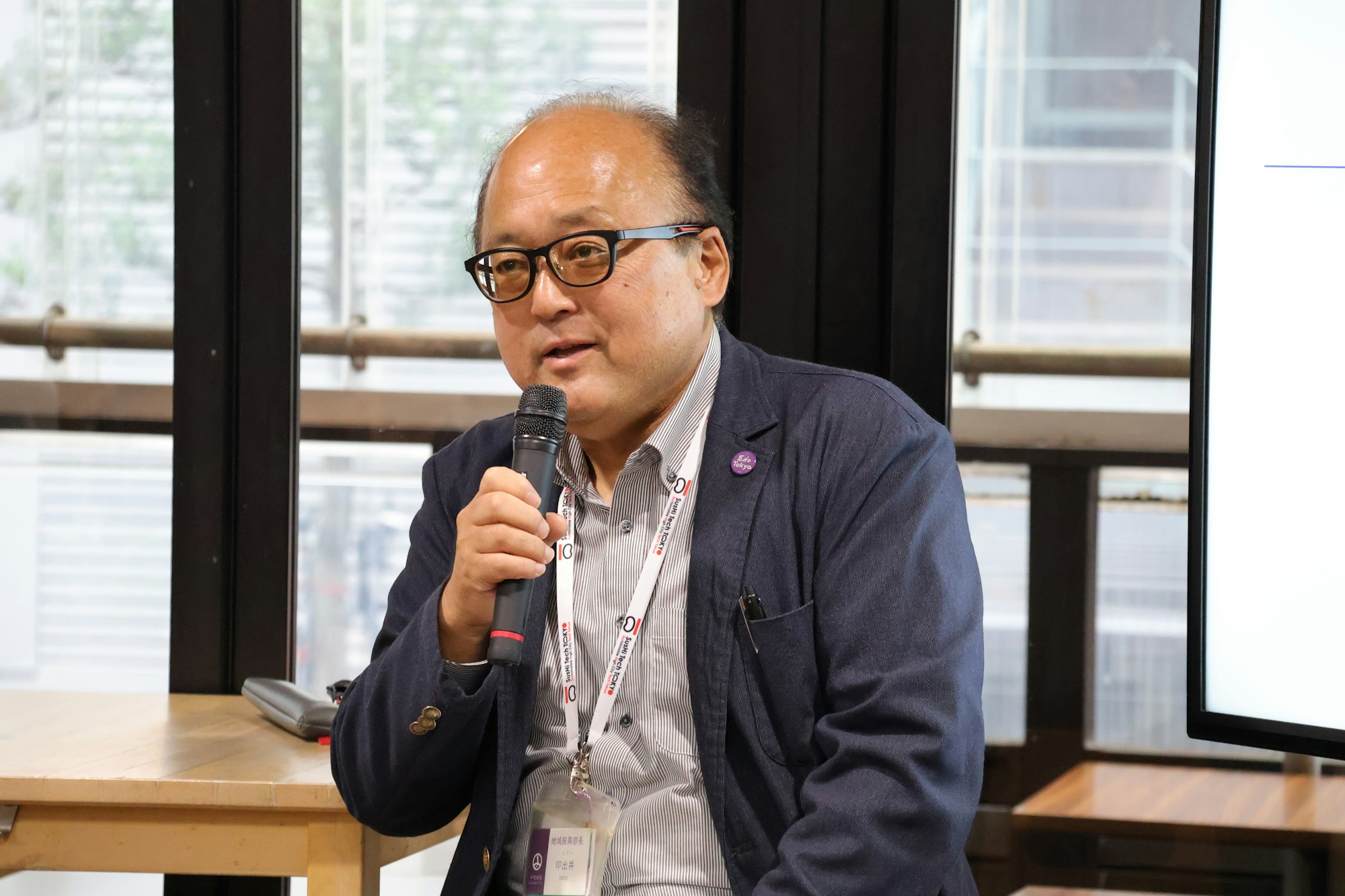 千代田区役所 地域振興部長 印出井 一美氏がマイクを手に登壇している写真