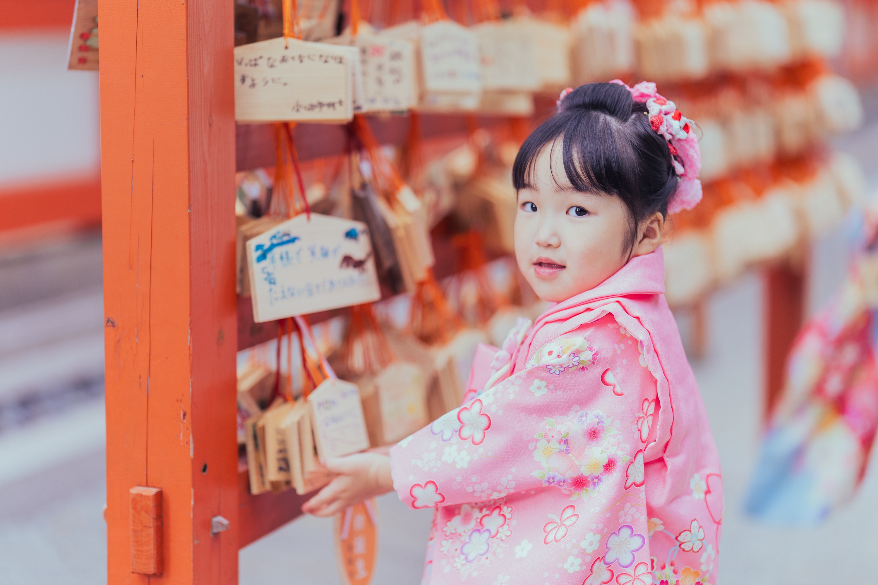 ピンクの着物の妹が絵馬の前で振り返っている