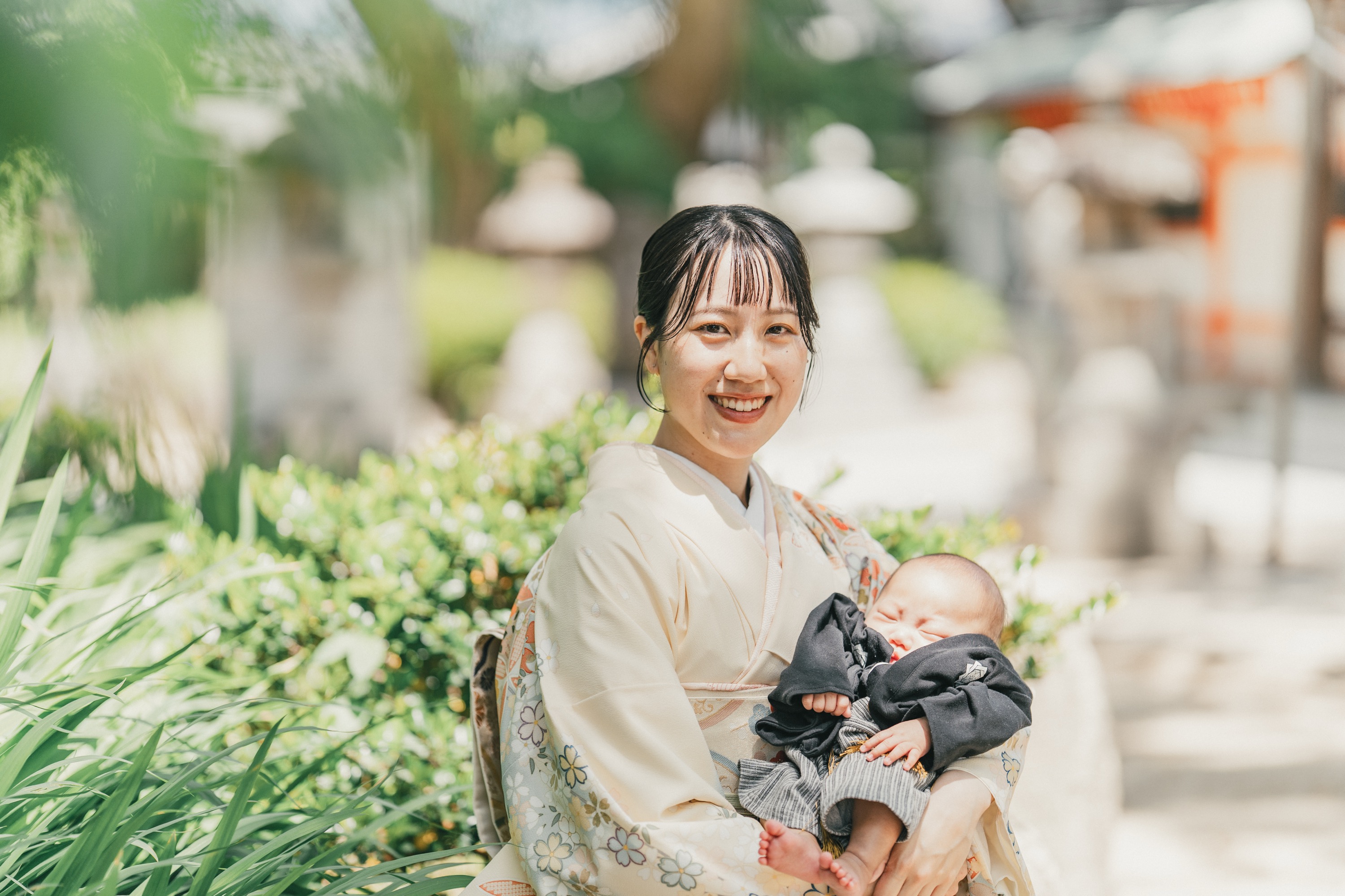 緑の植え込みの前で赤ちゃんを抱くお母さん