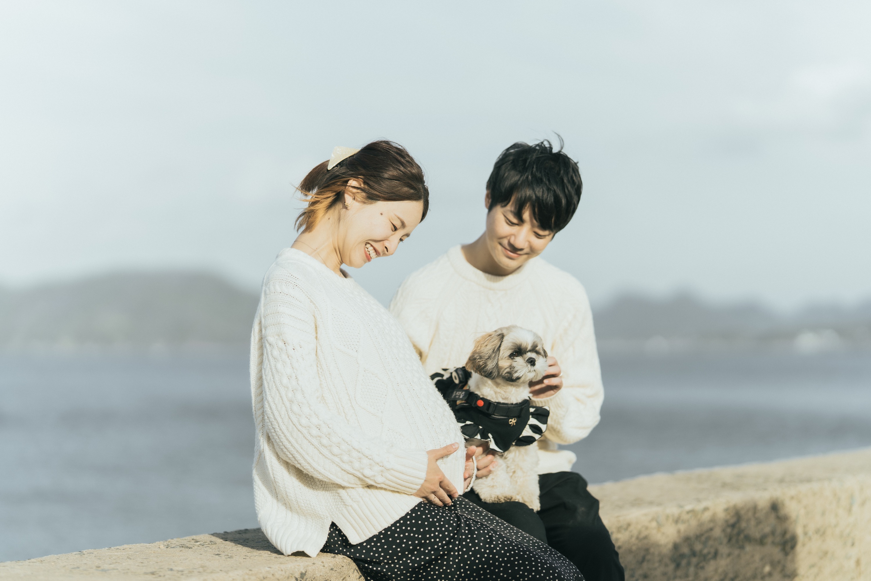 海辺の堤防に座り愛犬を抱える夫婦