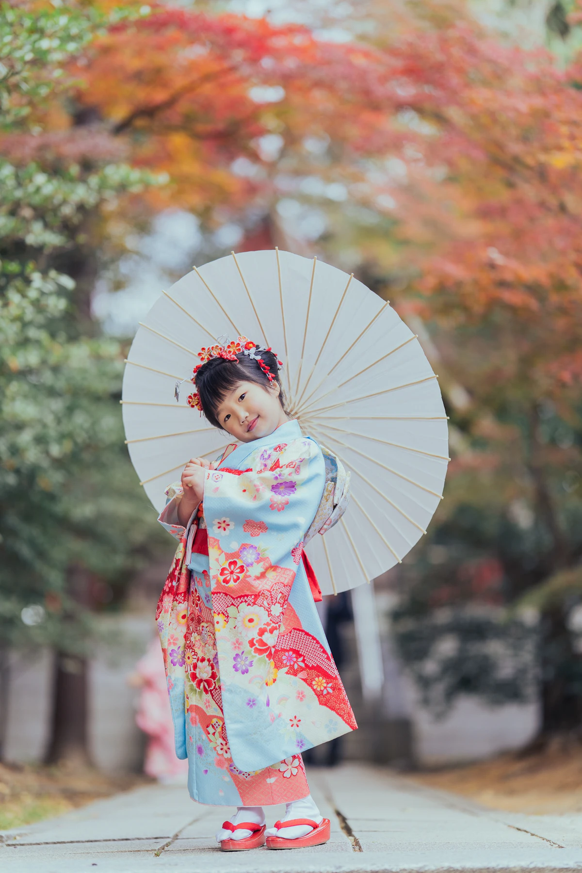 お姉ちゃんが和傘を持って紅葉の参道に立っている