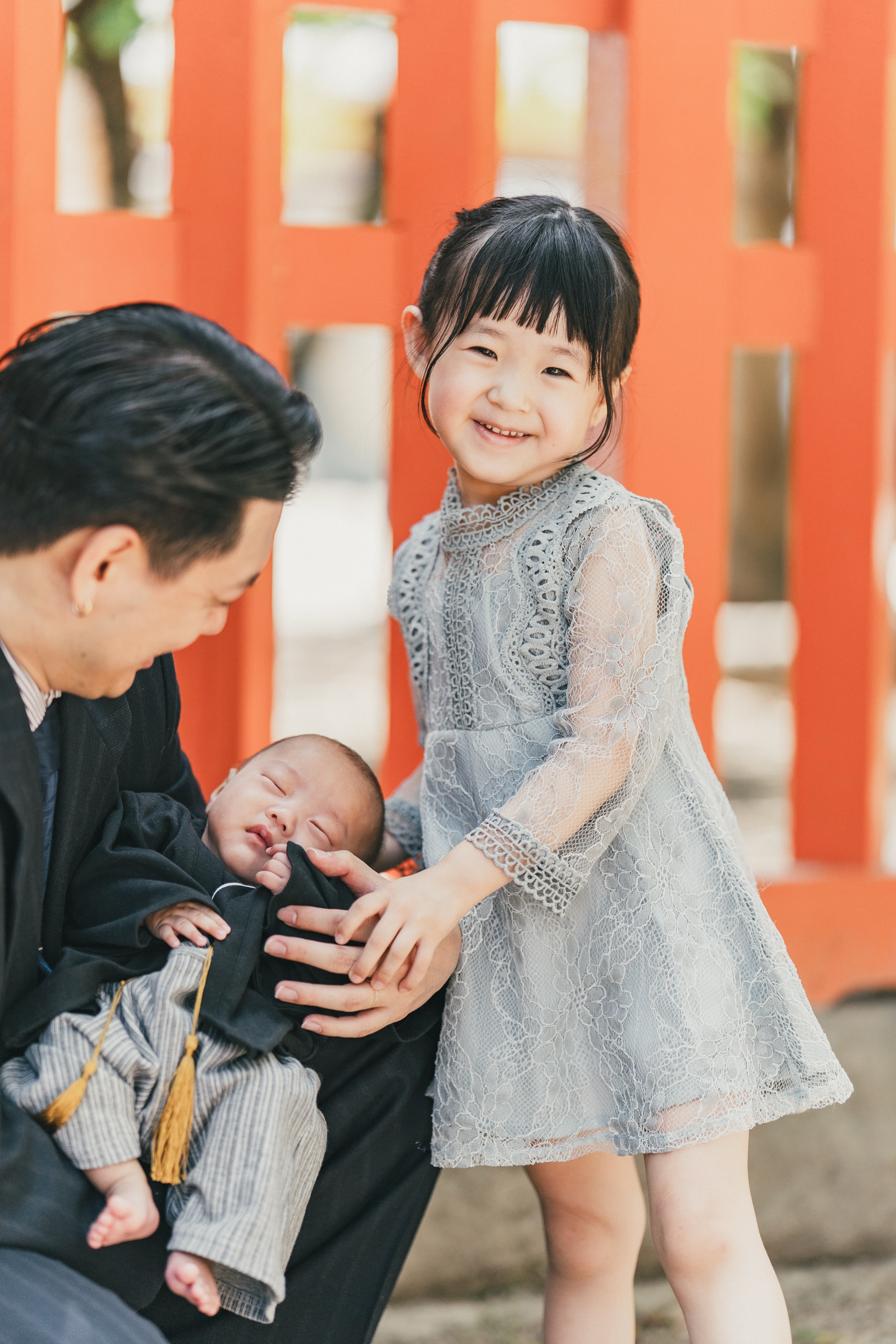 朱色の柵の前で弟にそっと手を添えて笑うお姉ちゃん