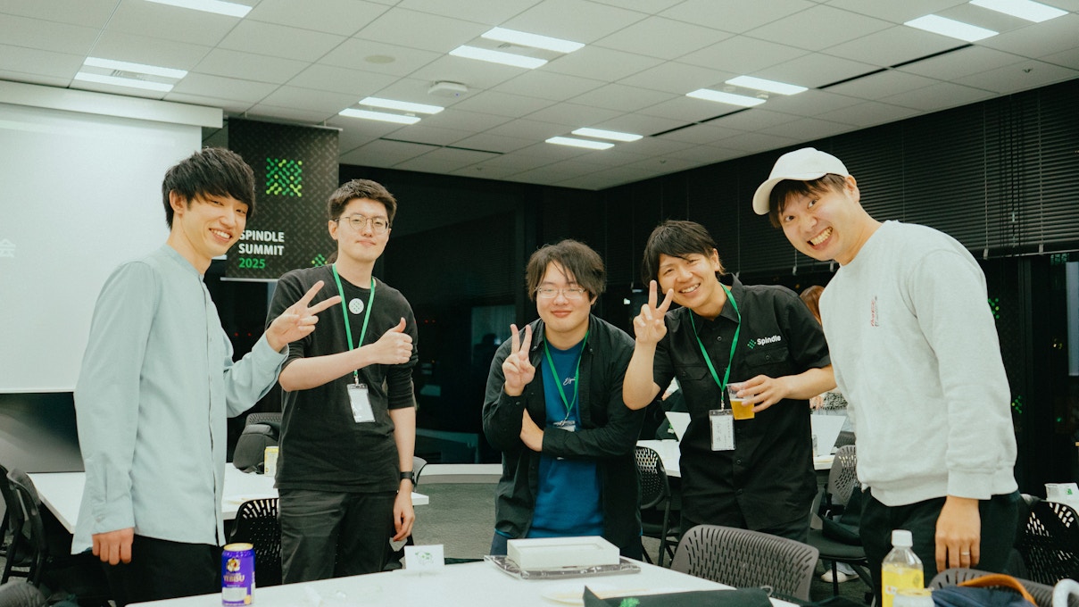 Spindle SUMMIT 2025の会場でポーズを取る5人の参加者。皆が笑顔でピースサインをしながらカメラに収まっている、懇親会の和やかな一コマ。
