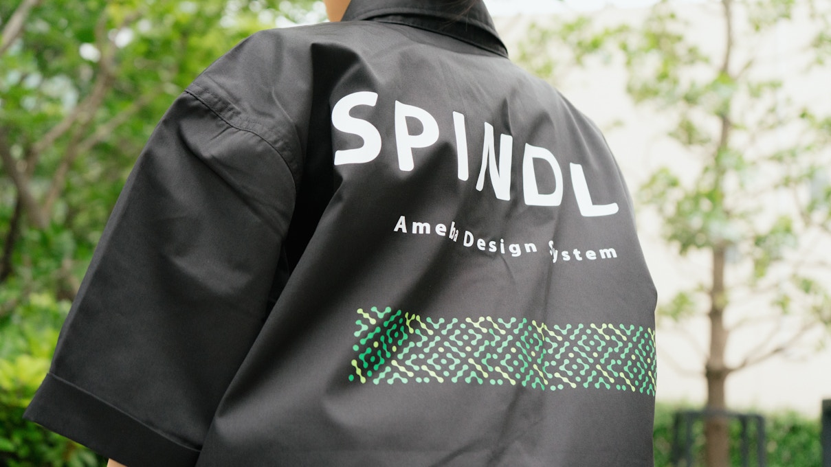Spindleのワークシャツ背面にあしらわれたロゴと「Ameba Design System」の文字が大きく写されたクローズアップショット。ブランドの力強さを感じさせる構図。