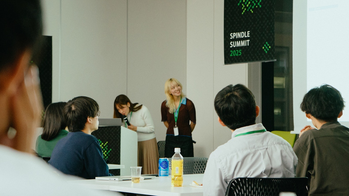 女性2人が登壇してプレゼンを行っている様子。1人がマイクを持ち、もう1人が笑顔で会場を見渡している。