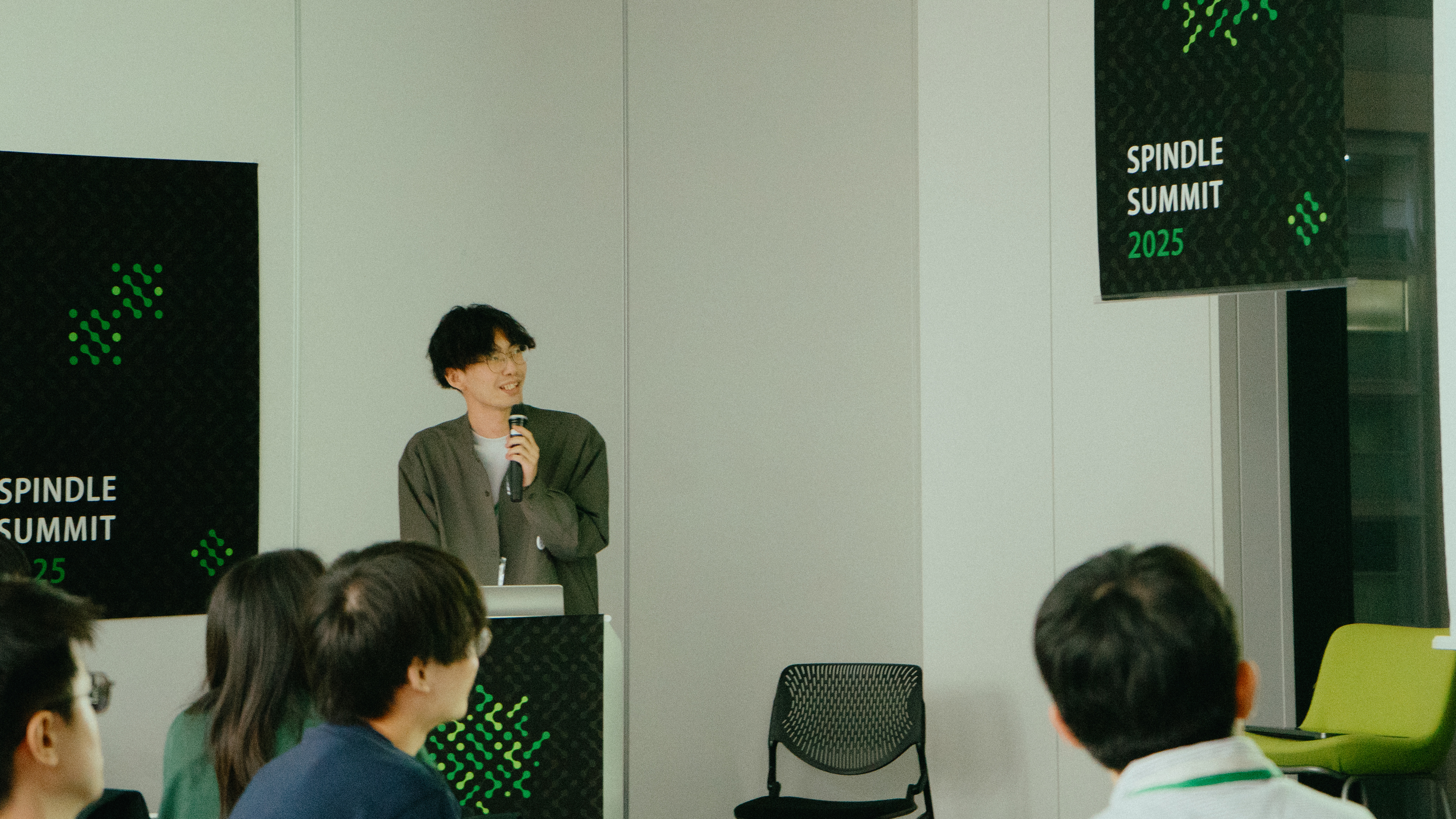 若い男性がスピーカーとして登壇しているシーン。手にマイクを持ち、笑顔で話している姿。