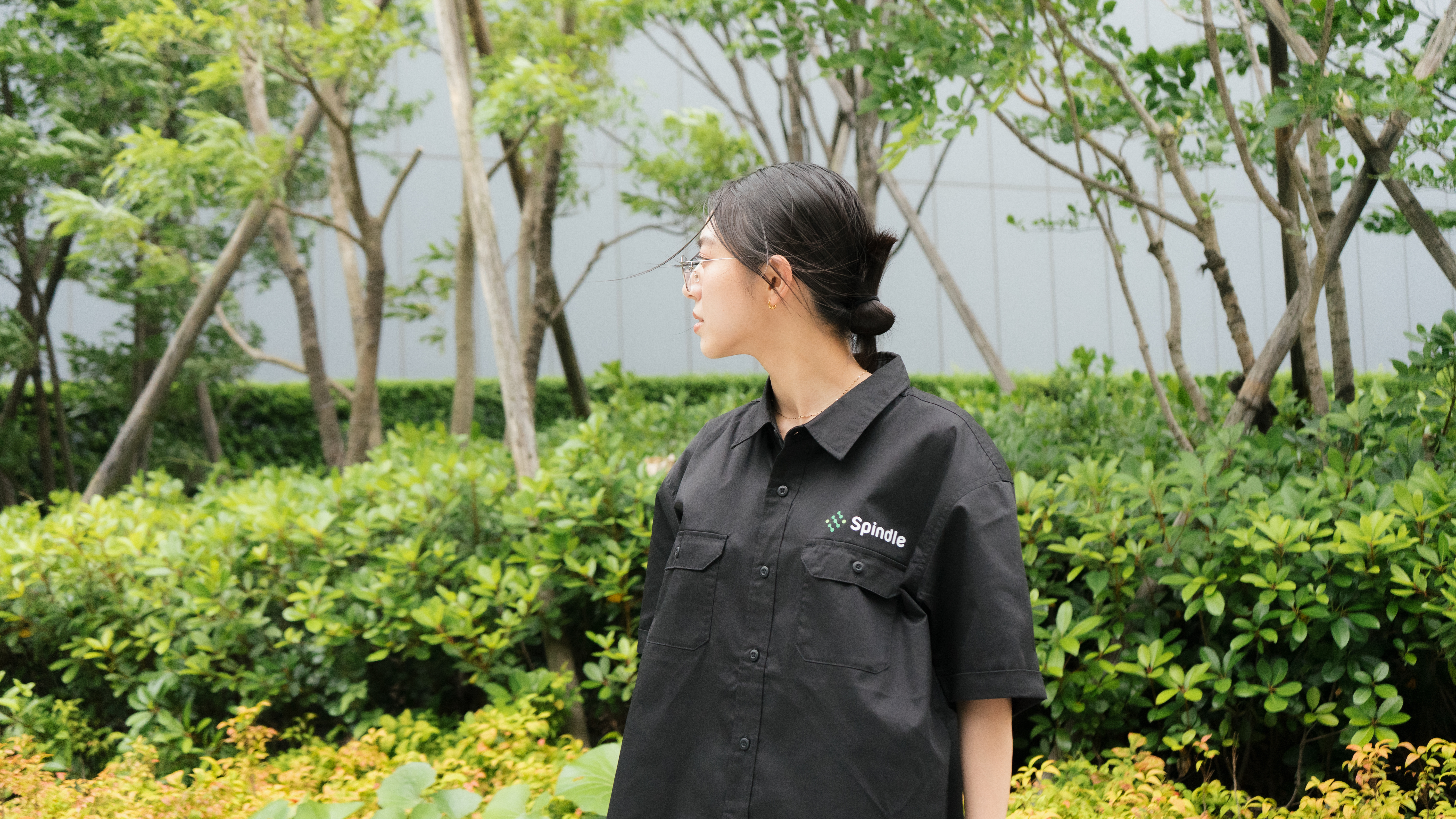 屋外でSpindleの黒いワークシャツを着た女性が横を向いて立っている姿。
