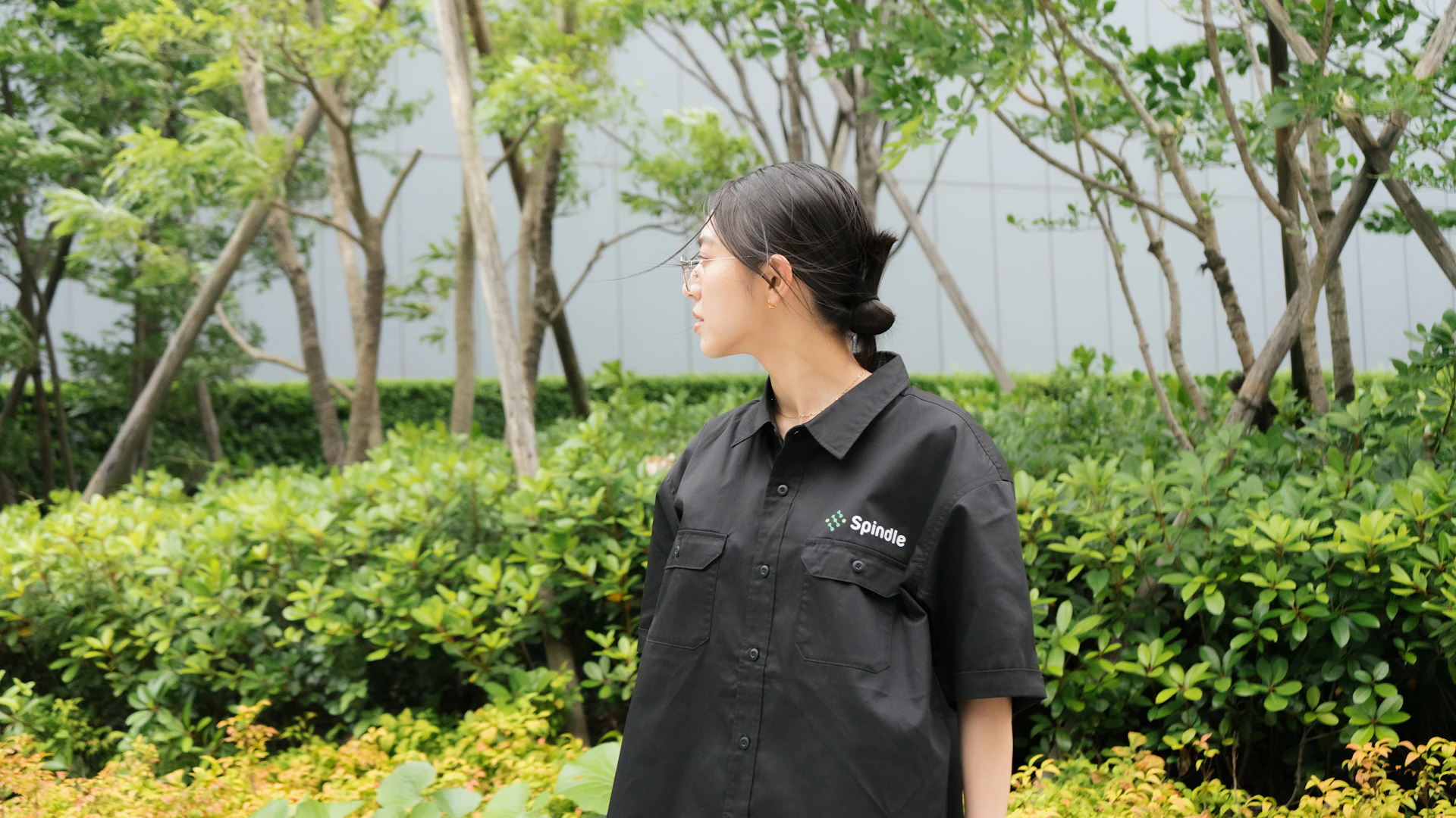 屋外でSpindleの黒いワークシャツを着た女性が横を向いて立っている姿。