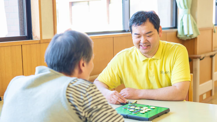 ご利用者とオセロを楽しむ障害者支援施設の介護職員の写真