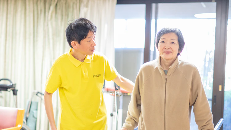 高齢者施設の介護職員がご利用者の歩行を支えている様子