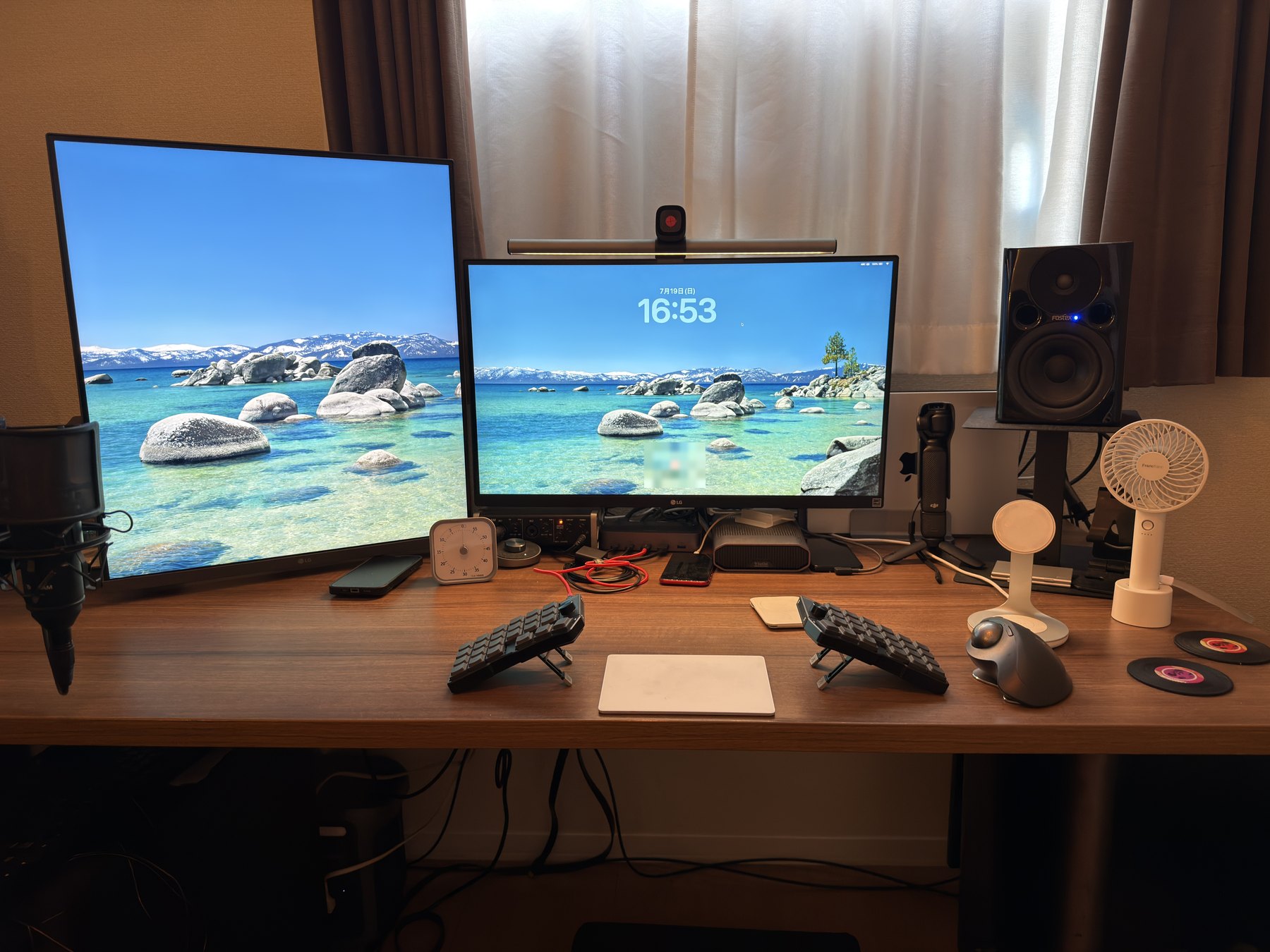 在宅デスクの全景。私用・社用の MacBook Pro 2 台を、1 組のモニター・キーボード・マウスに集約している(2026 年)