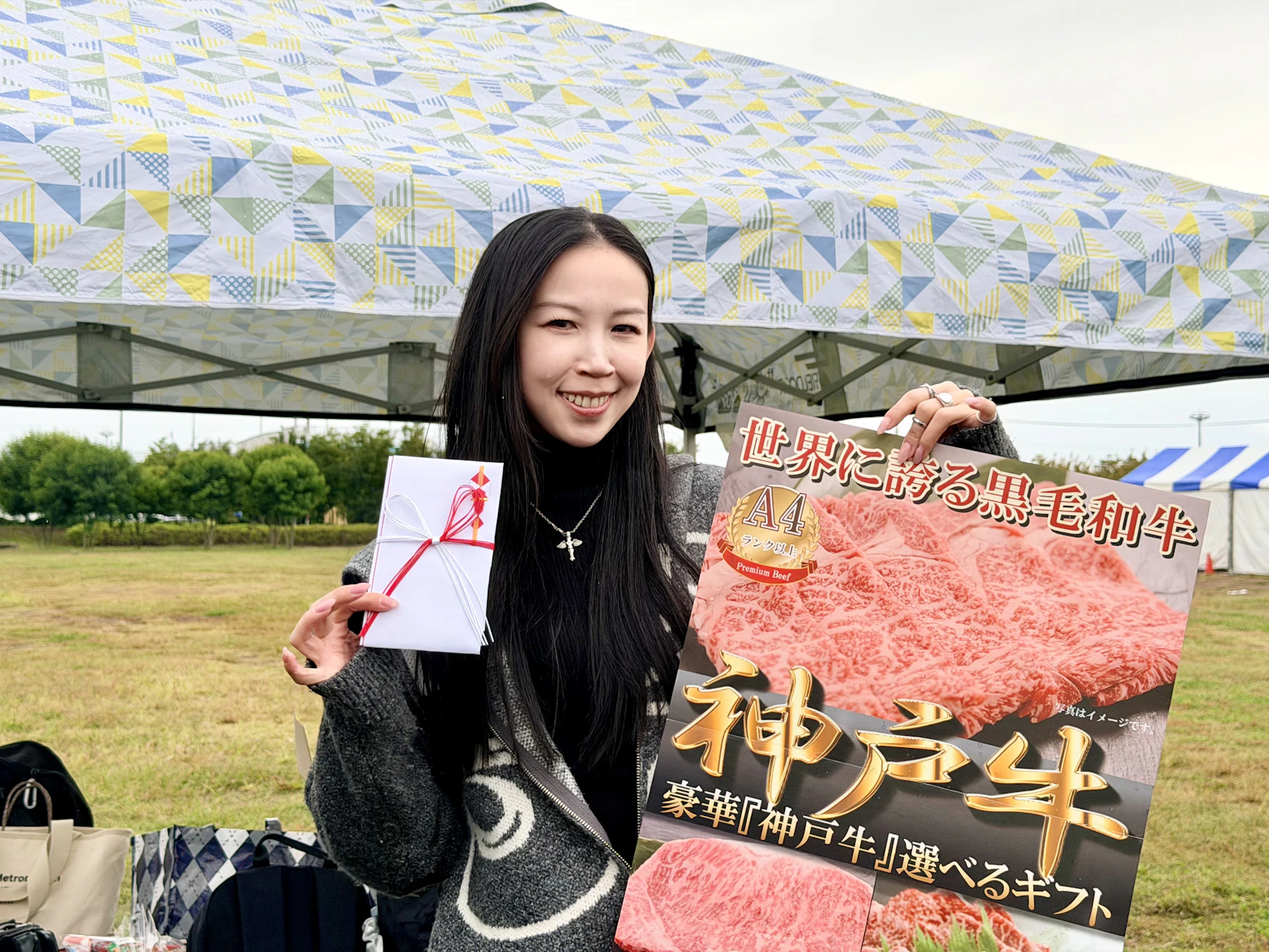 神戸牛と書かれた目録を片手にカメラに向かって微笑む酒井さん