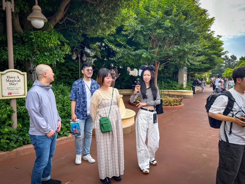 東京ディズニーシーのエントランス付近での集合の様子。社長はすでにディズニーキャラクターの形をしたカチューシャを身に着けている。朝早いながらもメンバーの顔には笑顔が見える。